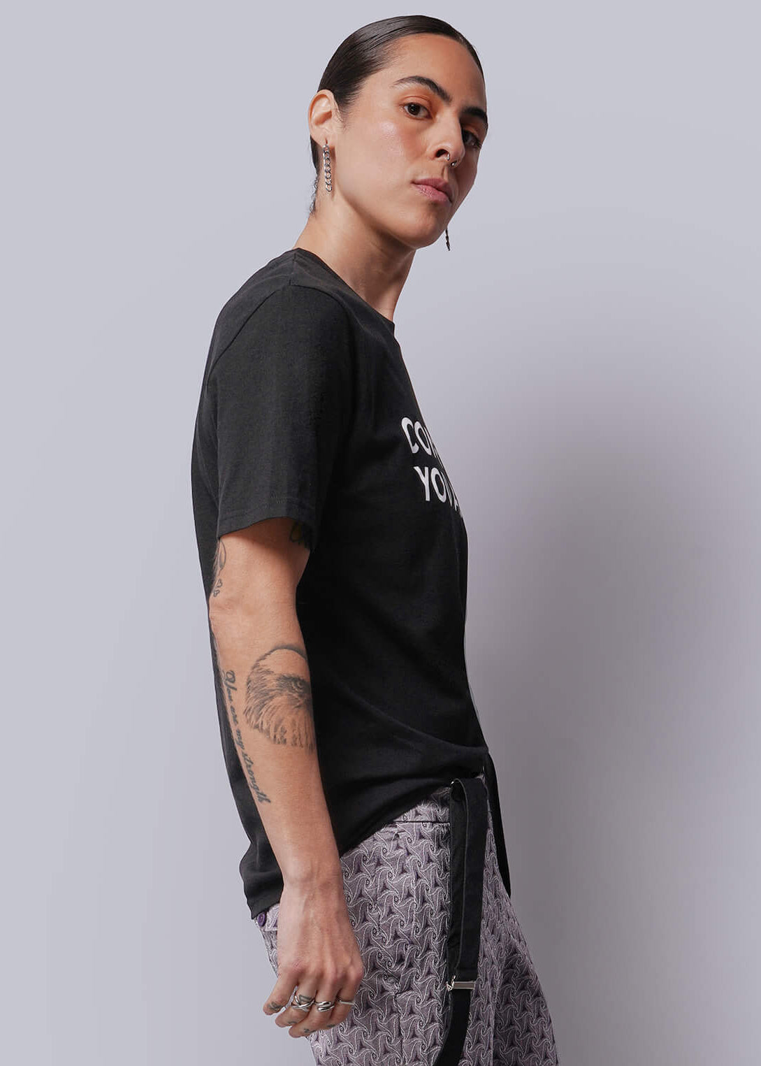 S=Person wearing a black t-shirt and patterned pants against a plain background