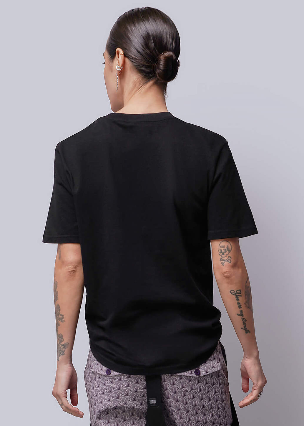 S=Person wearing a black t-shirt and patterned pants against a plain background