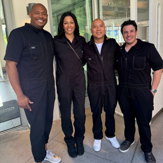 Group of people in black coveralls posing together in a modern indoor setting with large windows.