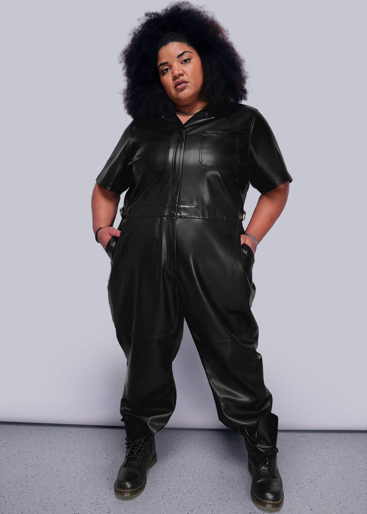 1X=Person wearing a black vegan leather jumpsuit against a plain background
