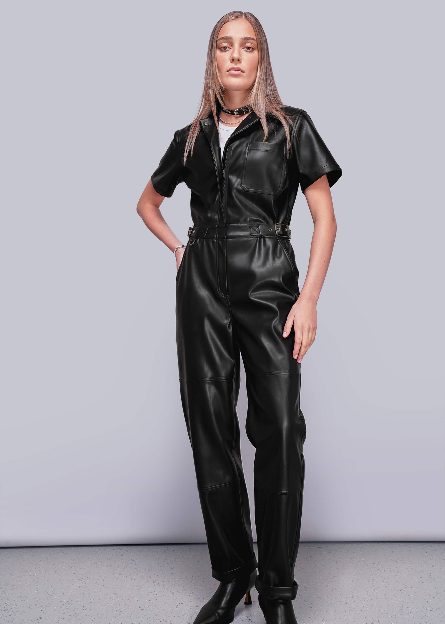 S=Person wearing a black vegan leather jumpsuit against a plain background