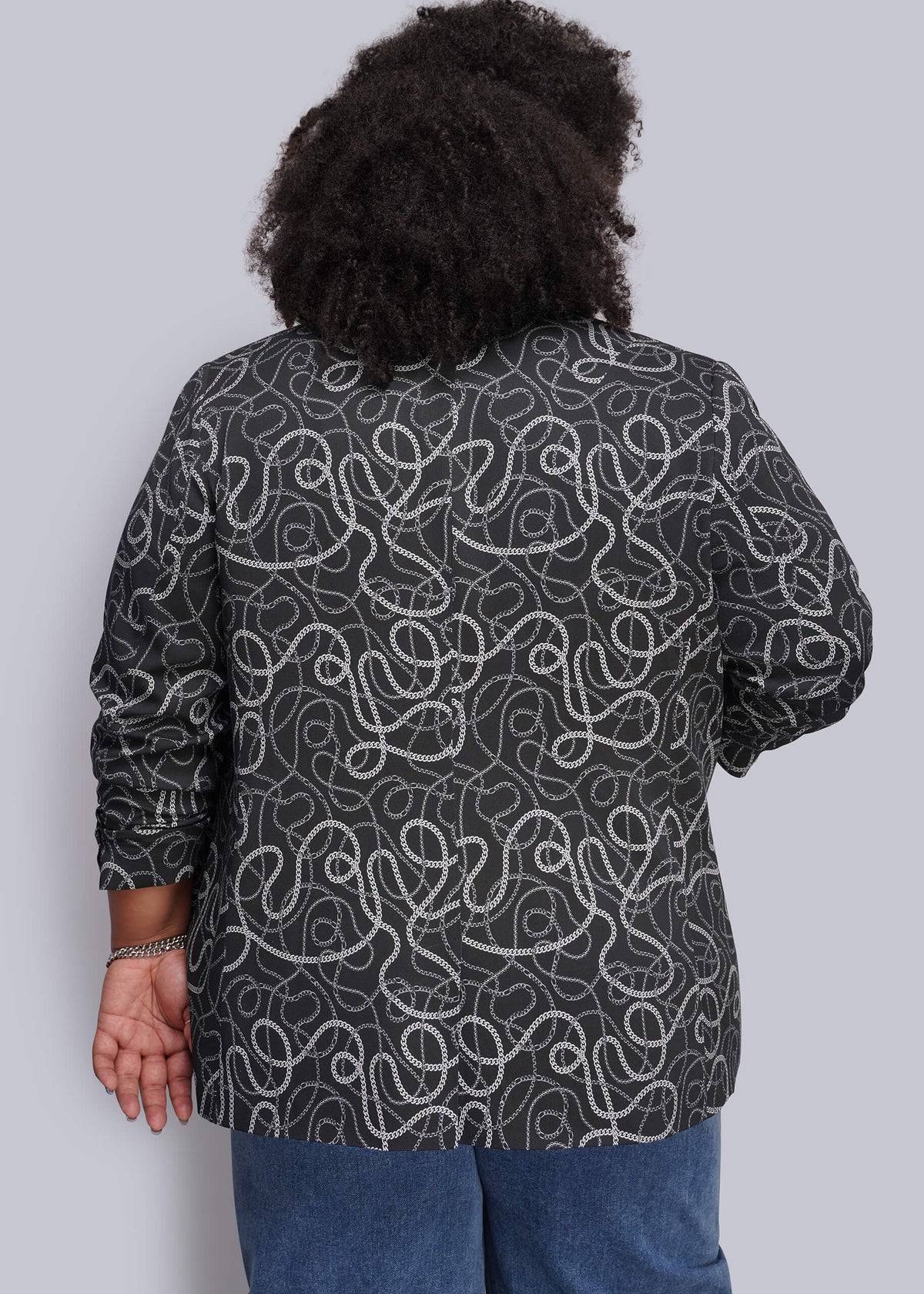 1X=A person viewed from the back wearing a dark charcoal gray long-sleeve button-up shirt with a white abstract chain pattern, paired with blue jeans, against a solid light gray background.