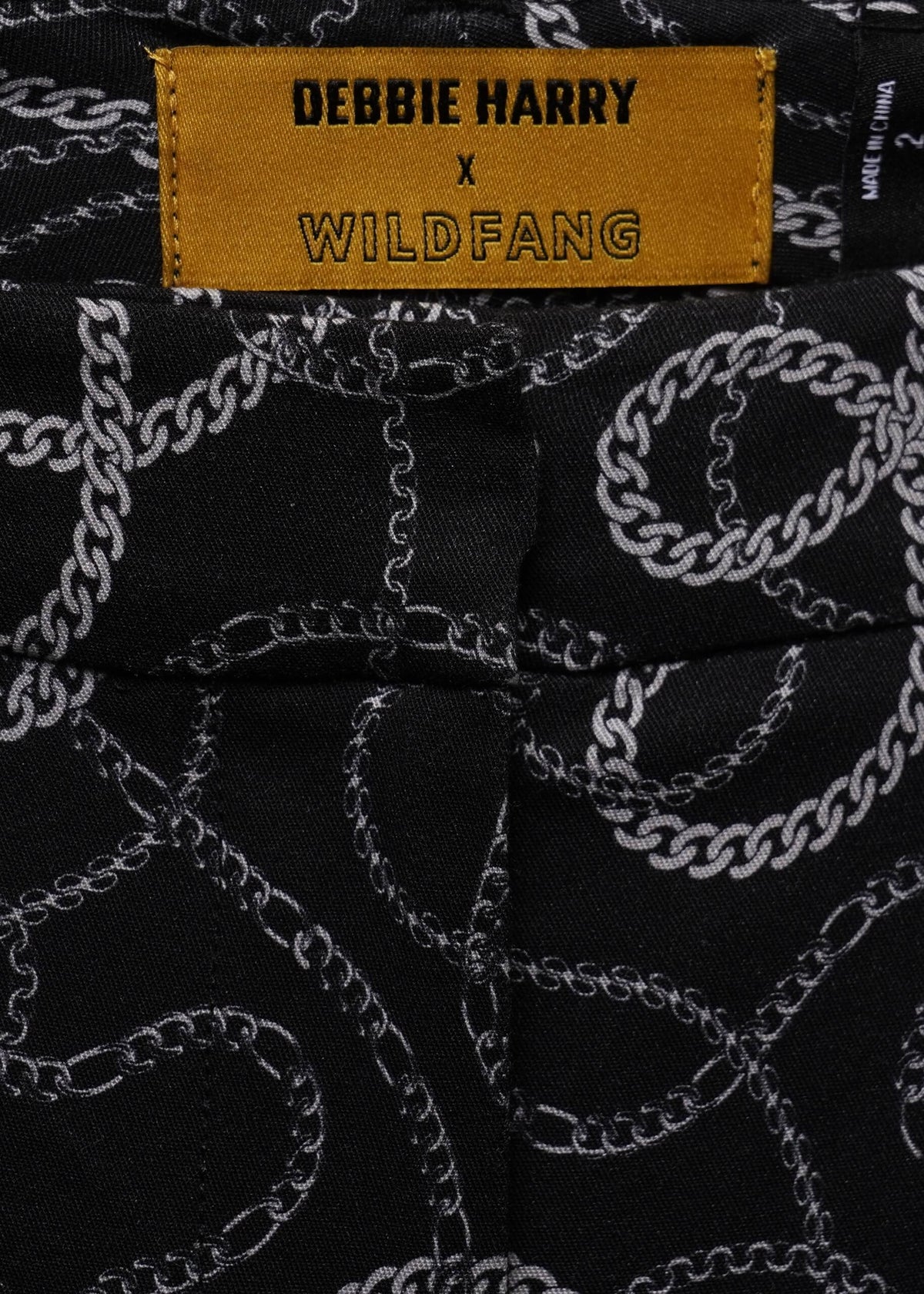 Close-up of black fabric with a white chain pattern and a yellow label reading 'DEBBIE HARRY x WILDFANG'.