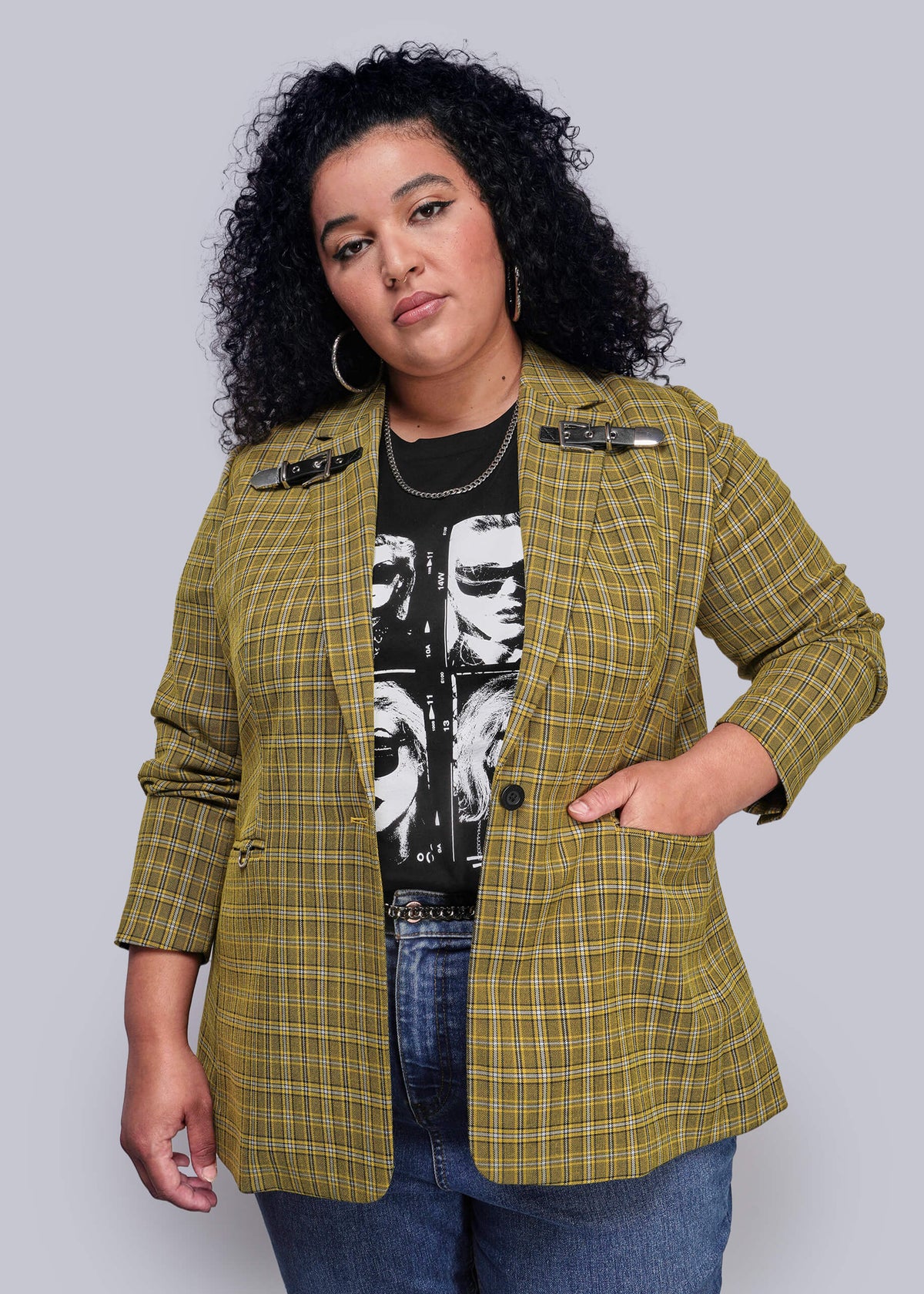 1X=Woman wearing a yellow plaid blazer over a black graphic t-shirt on a plain background