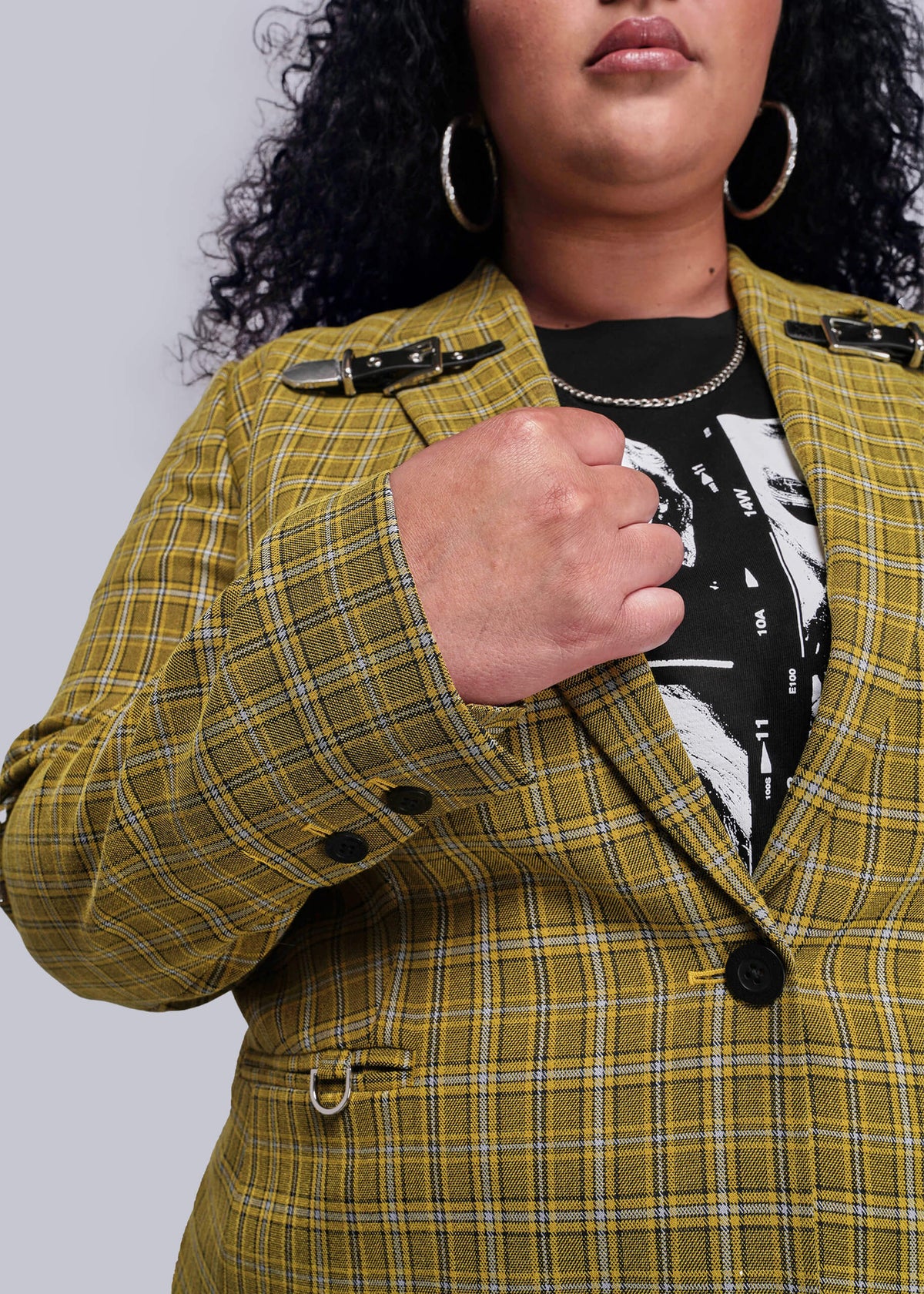1X=Close up view of person wearing a yellow plaid jacket with black buttons on a plain background