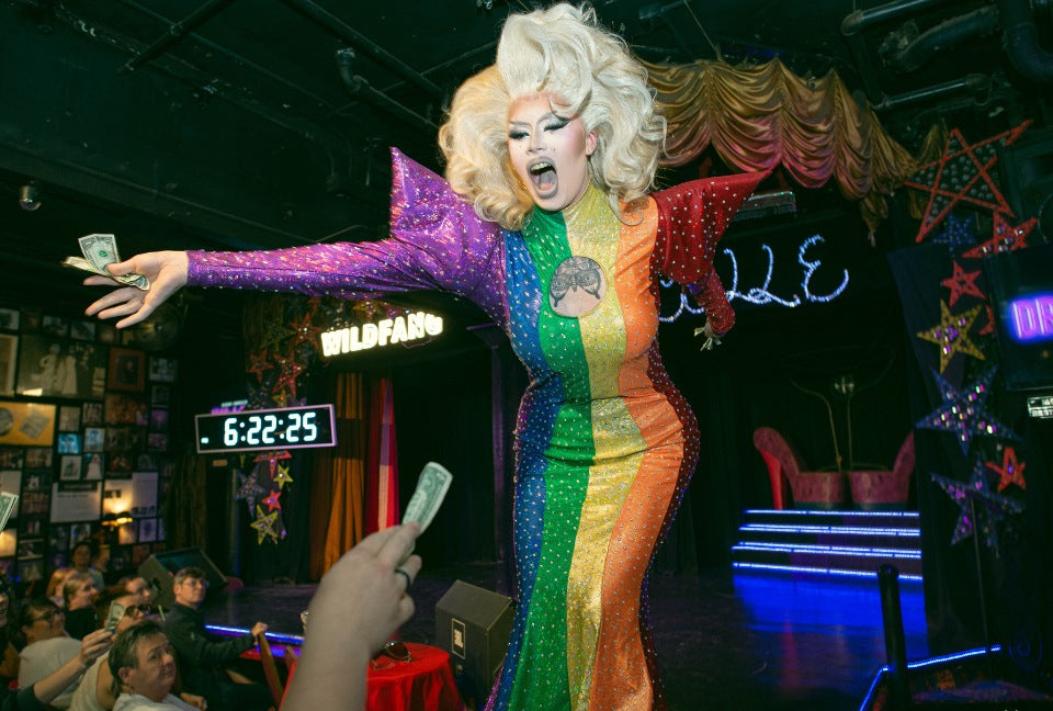 Drag queen wearing rainbow dress performs in front of audience while on stage at Darcelle's in Portland
