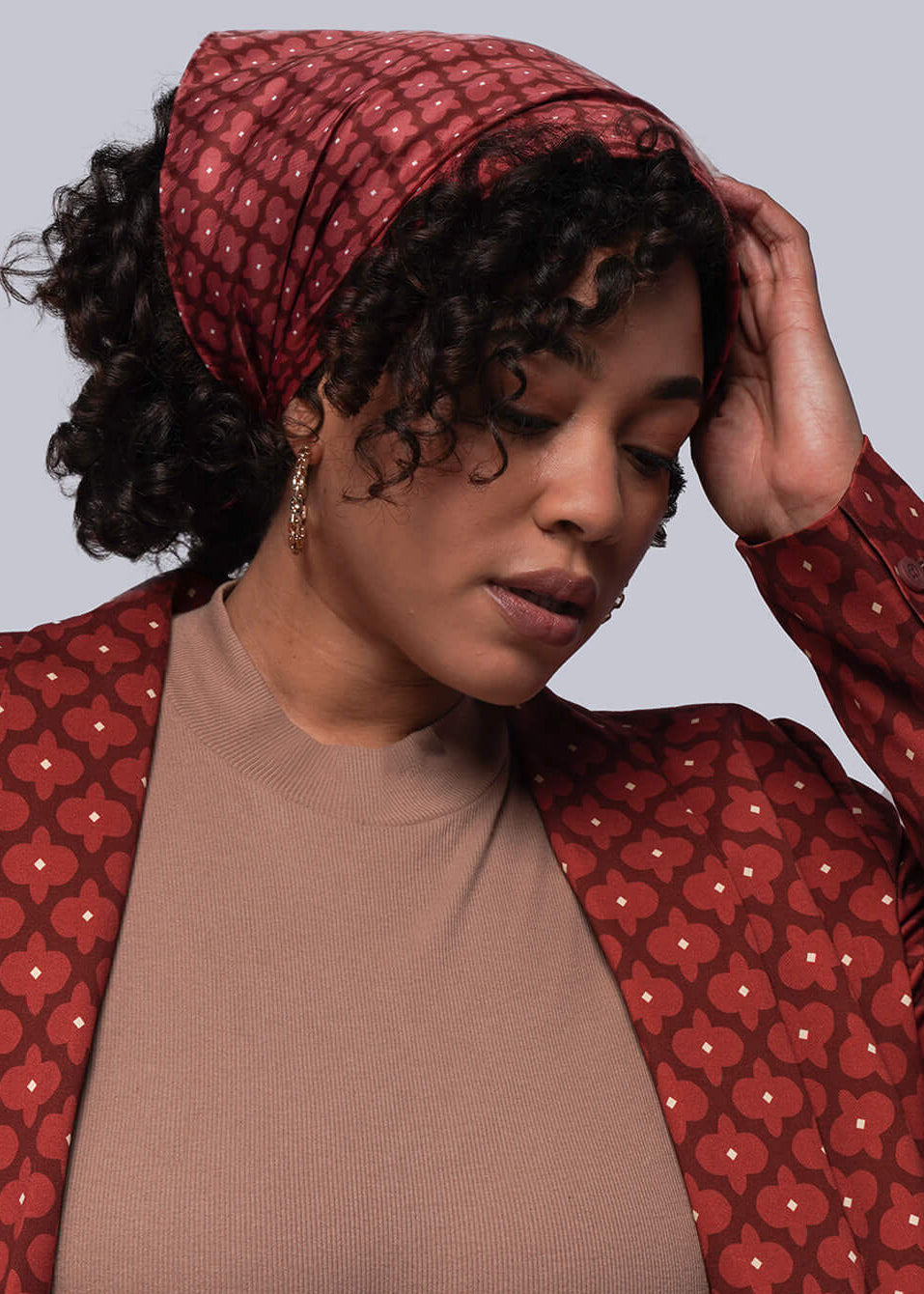 Person wearing a red patterned jacket over a brown top and blue jeans on a gray background