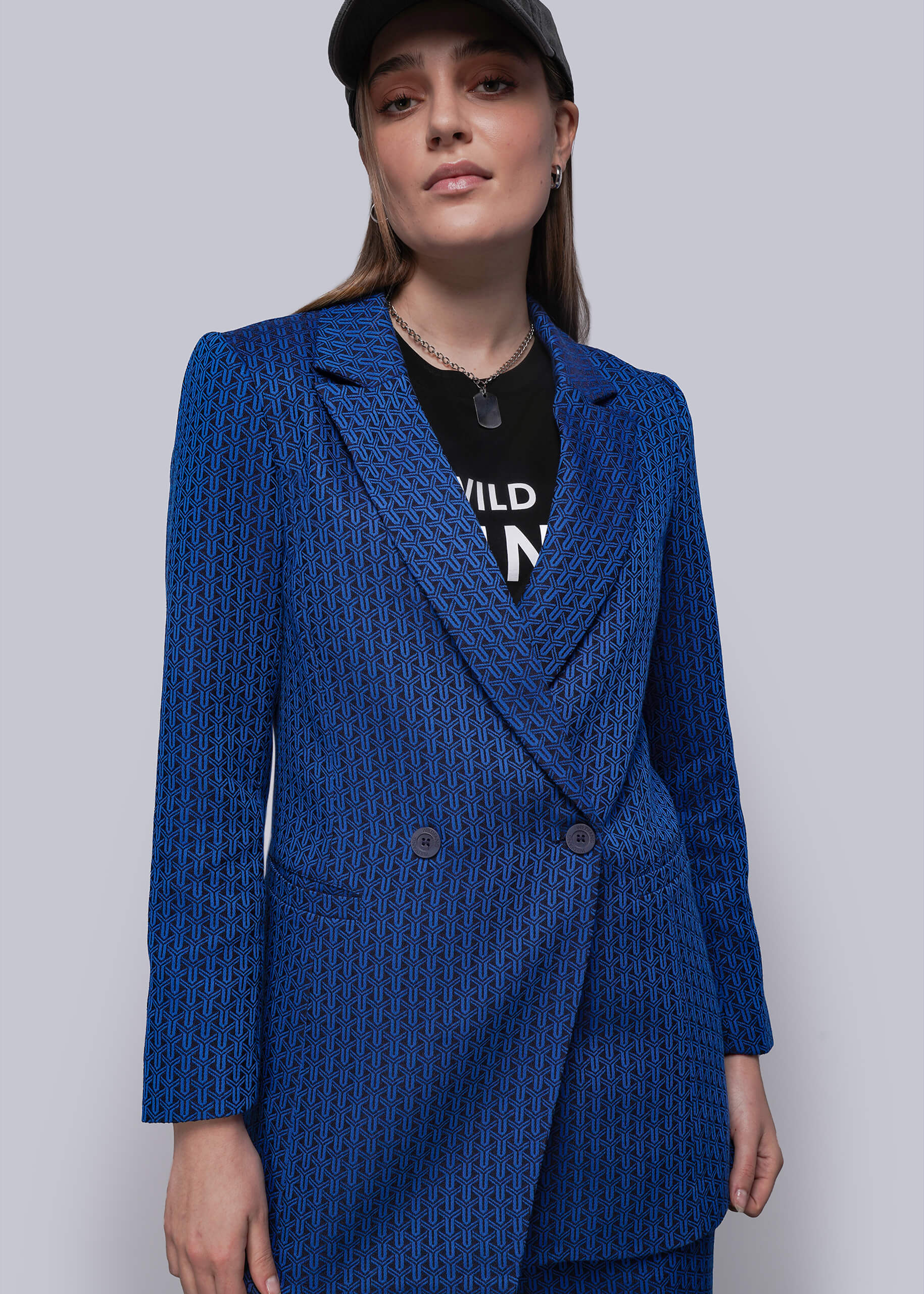 Woman wearing a blue textured blazer over a black outfit with visible text on a plain background