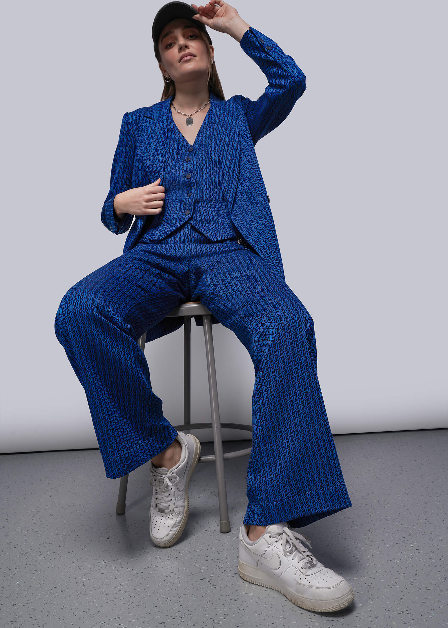 S=Person wearing a blue suit sitting on a stool against a plain background
