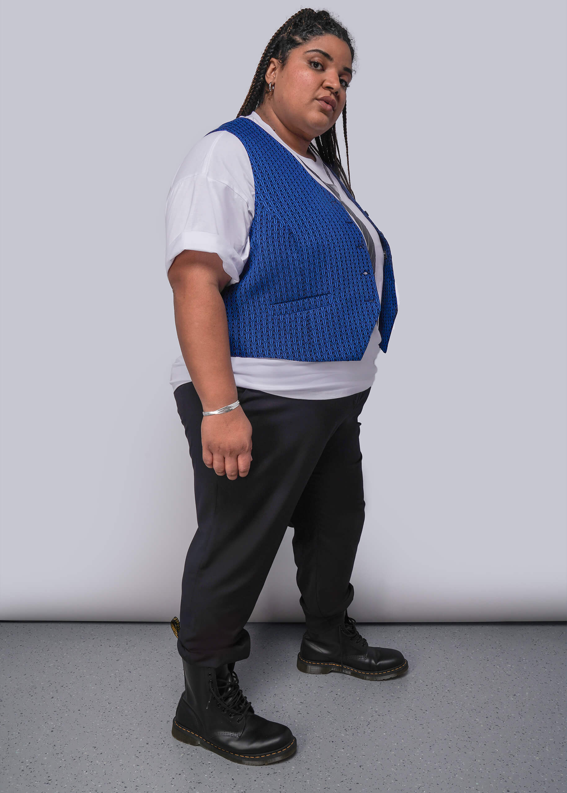 1X=Person wearing a blue vest over a white shirt with black pants and boots on a plain background