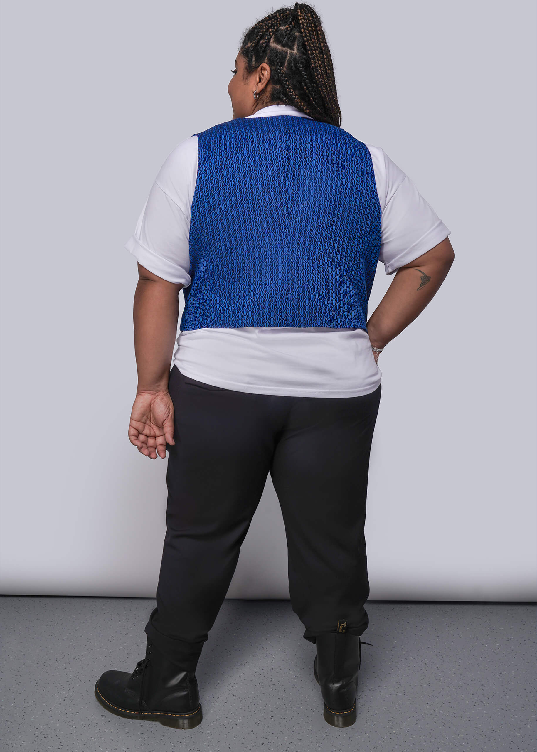 1X=Person wearing a blue vest over a white shirt with black pants against a plain background