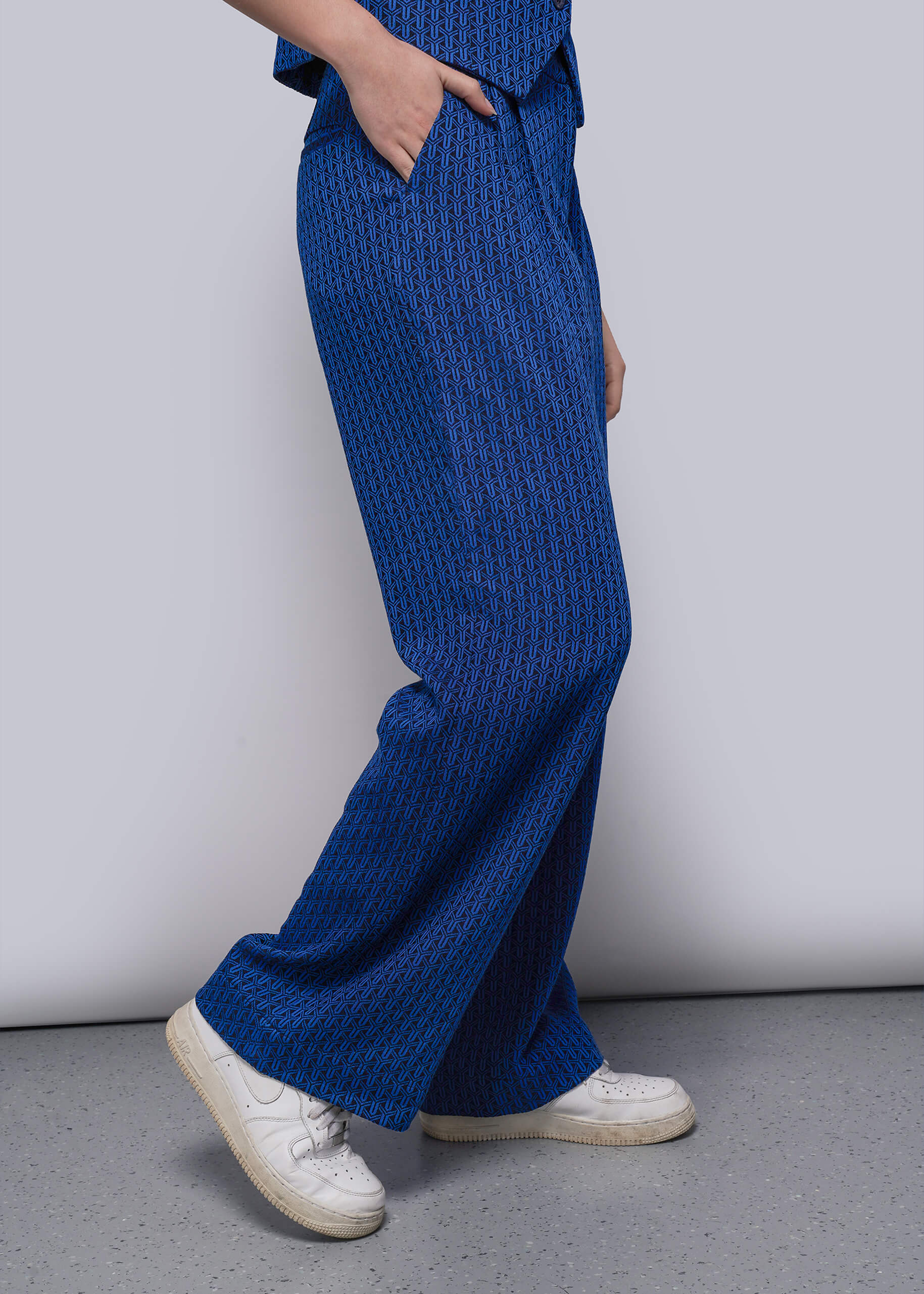 S=Person wearing blue textured pants and white sneakers against a plain background