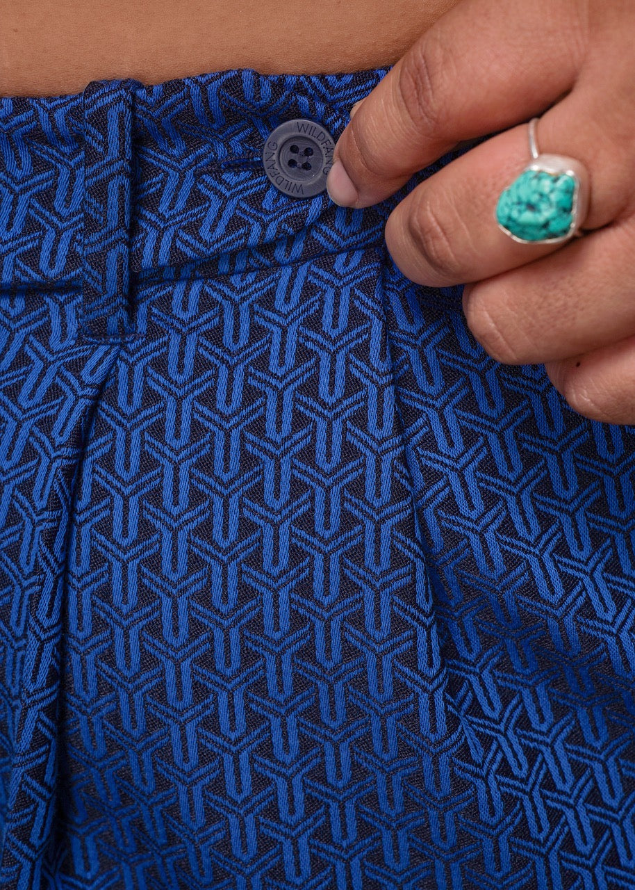 1X=Close-up of a person wearing blue pants with a button and turquoise ring.