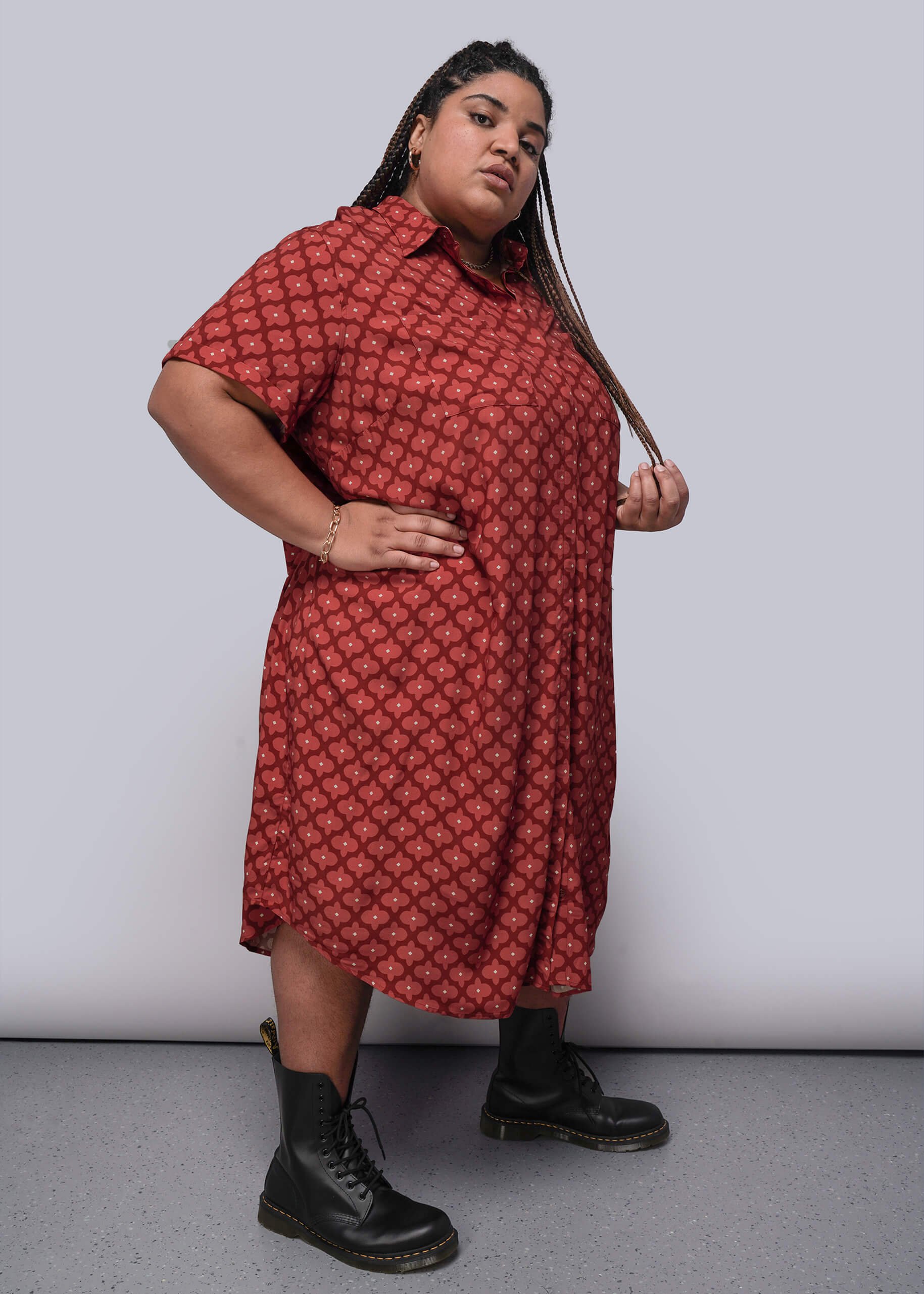 1X=Person wearing a red patterned dress with black boots against a plain background