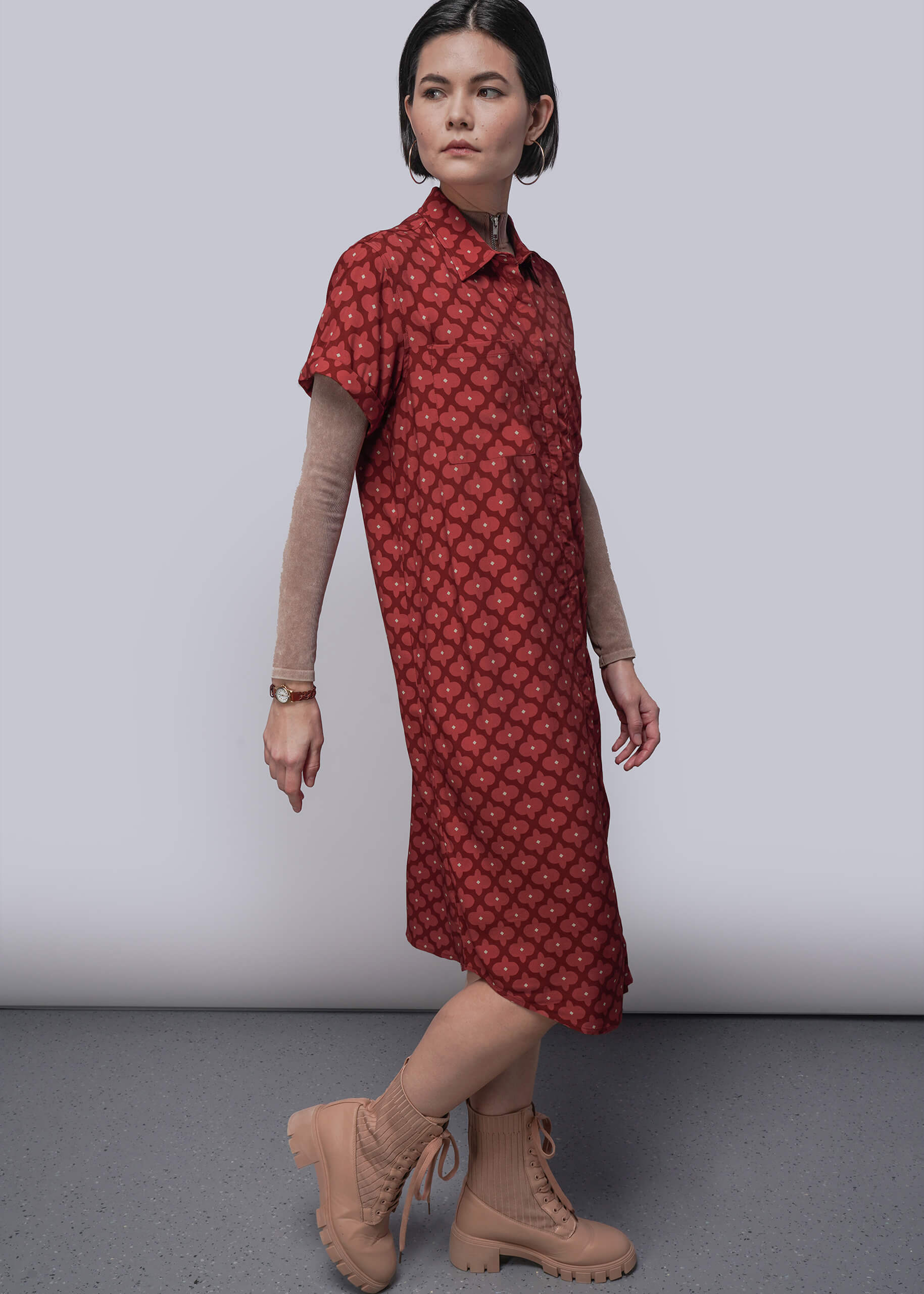 S=Woman wearing a red patterned dress with beige boots on a plain background