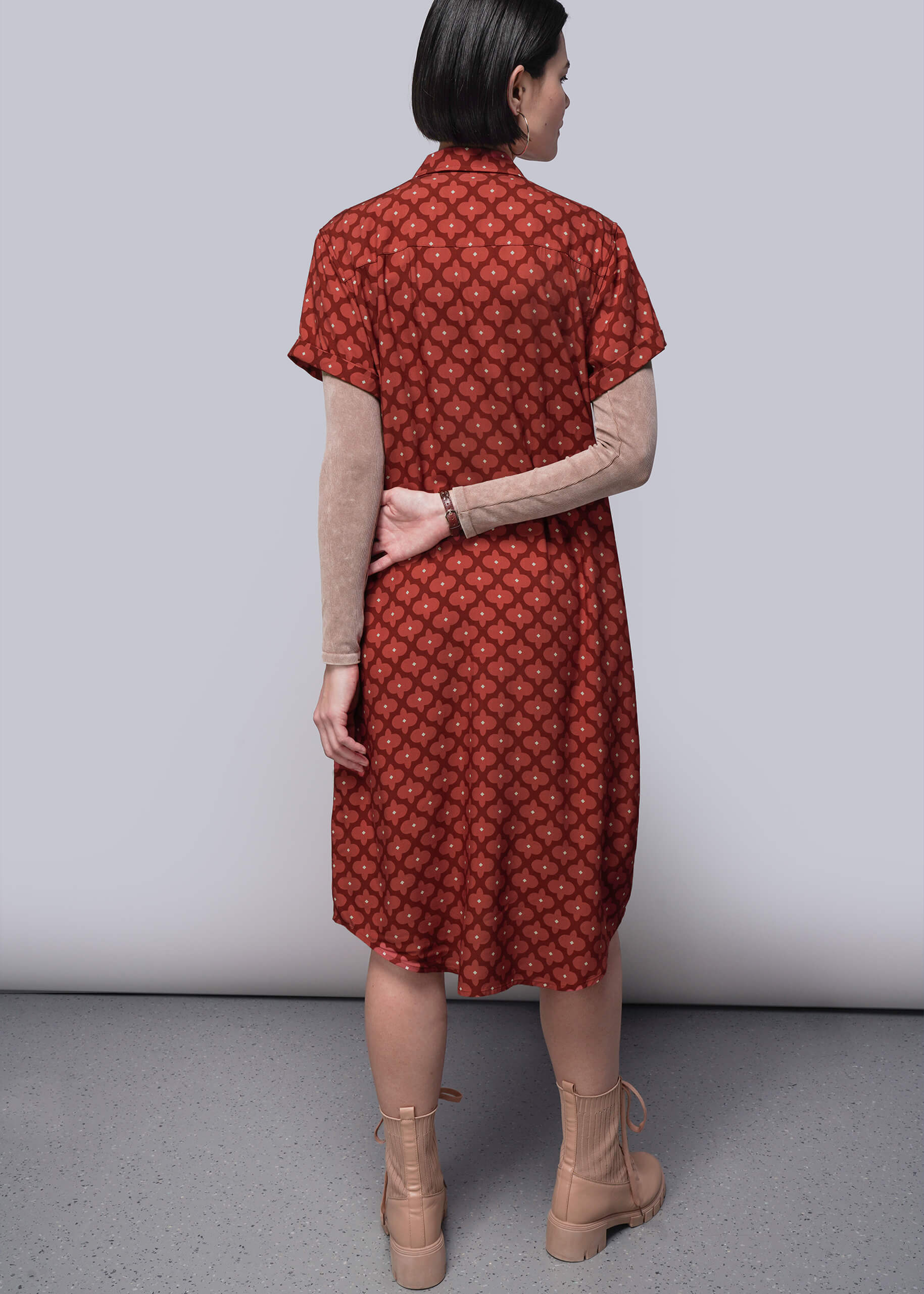S=Woman wearing a red patterned dress with beige boots on a plain background