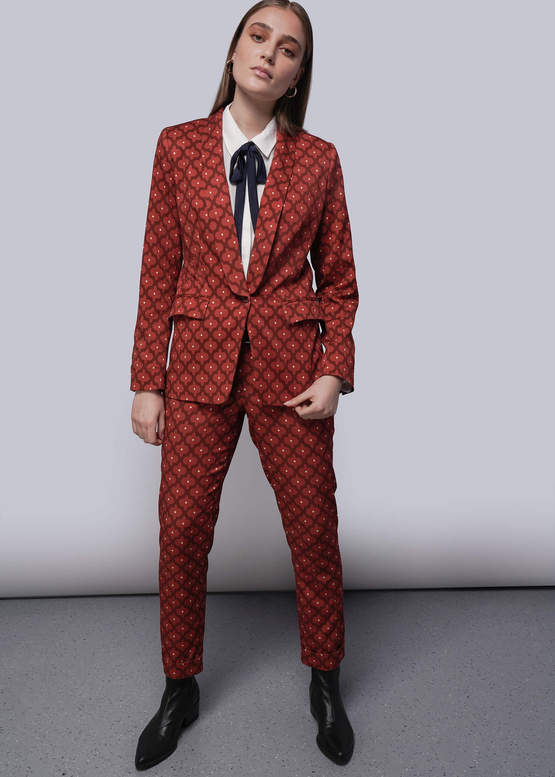 Person wearing a red patterned suit with a white shirt and black shoes on a plain background