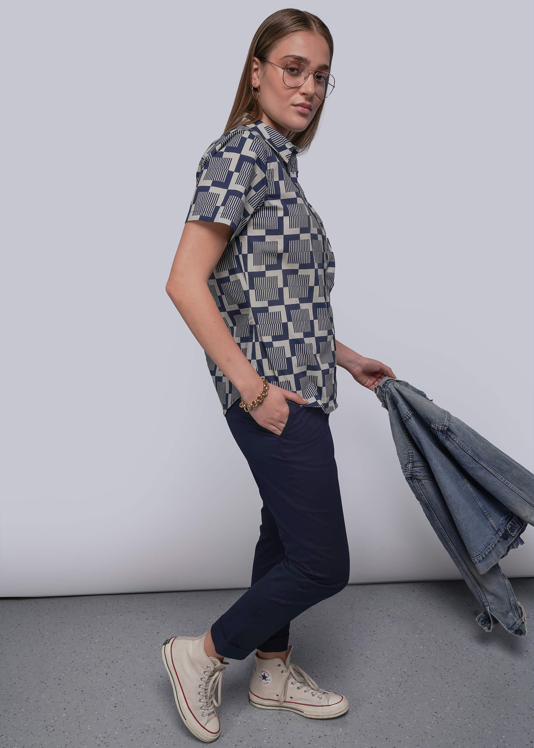S=Person wearing a patterned shirt and dark pants, holding a denim jacket against a plain background