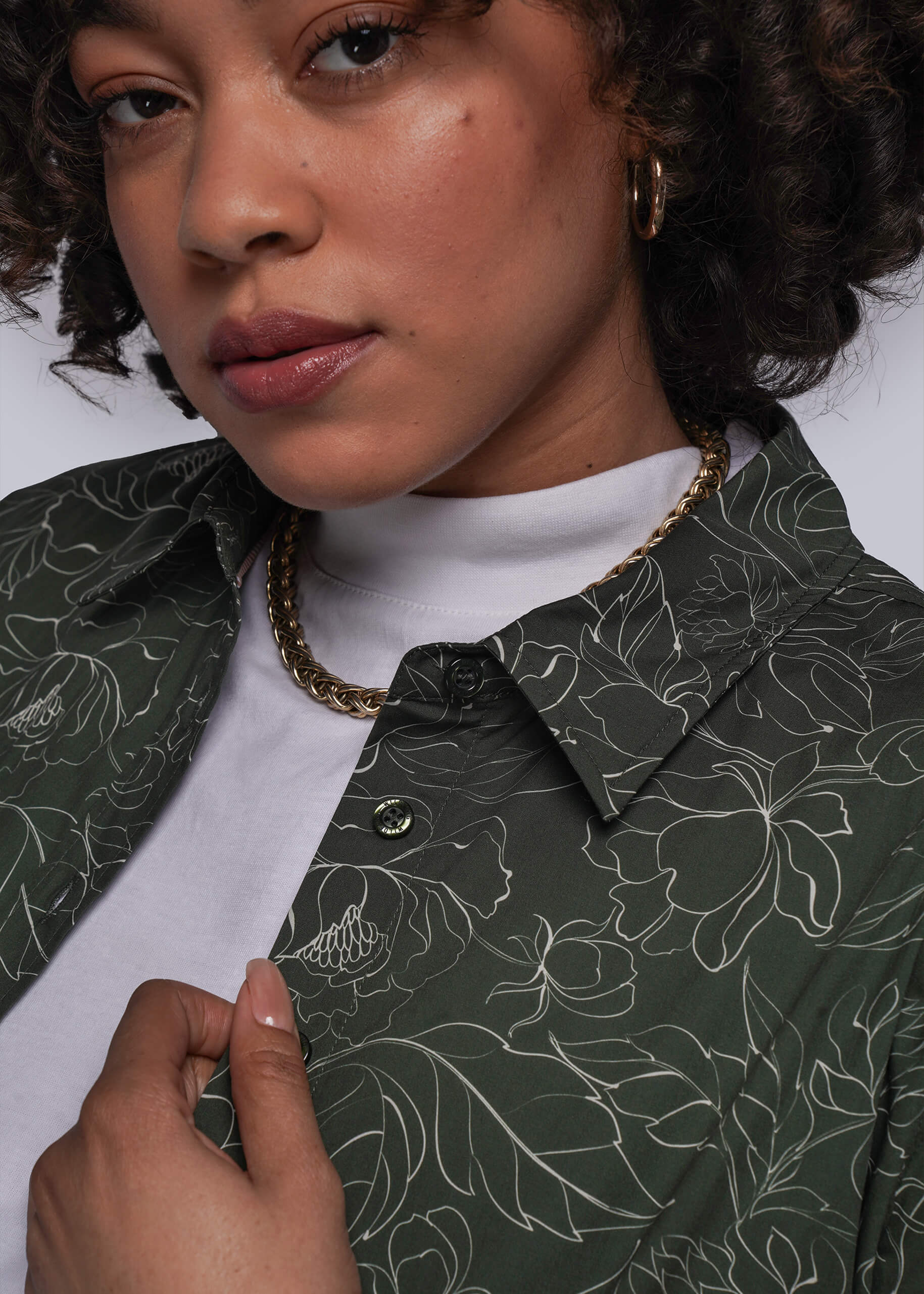 1X=Person wearing a dark green floral-patterned shirt with a white turtleneck underneath.