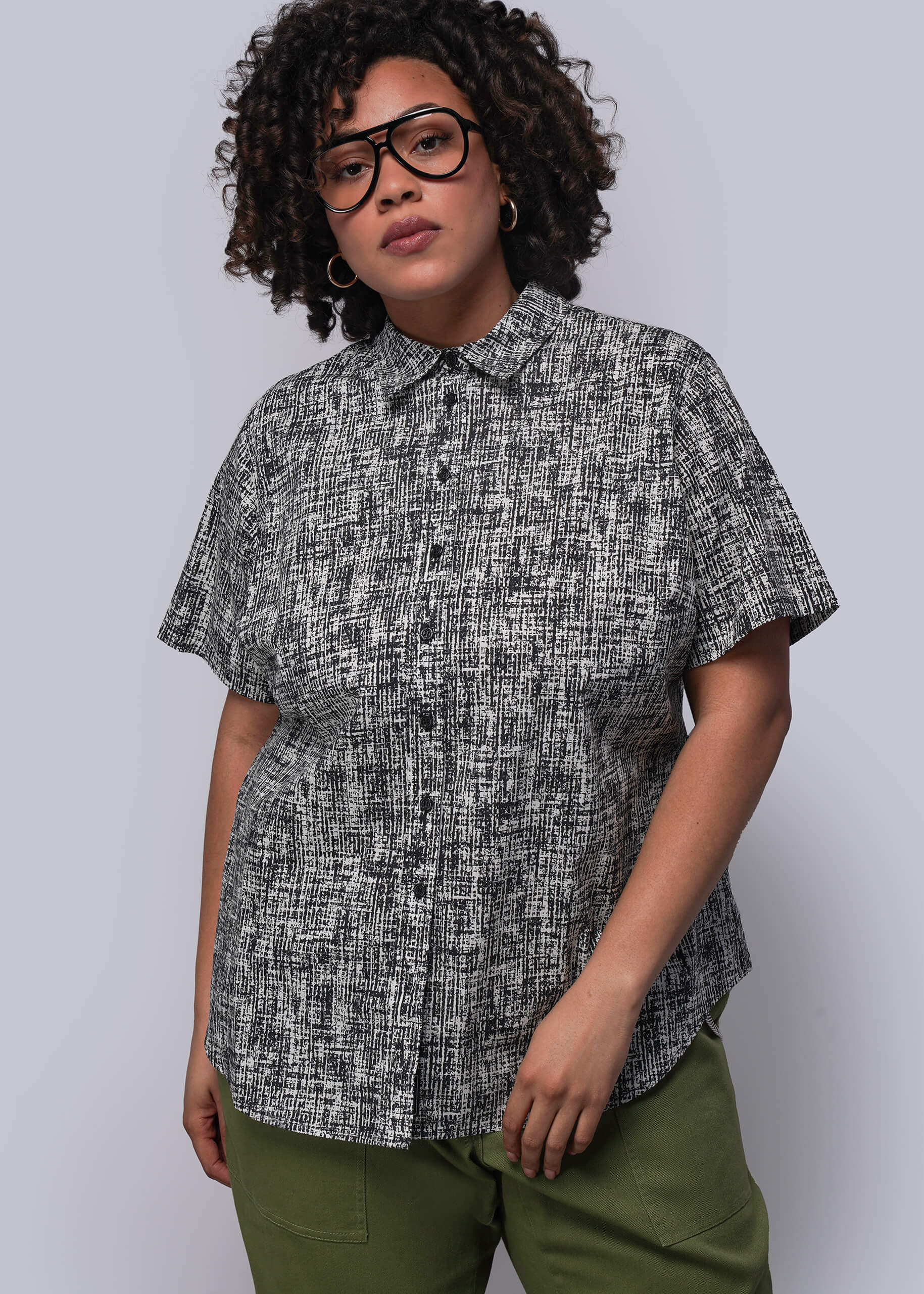 1X=Person wearing a patterned shirt and green pants against a plain background
