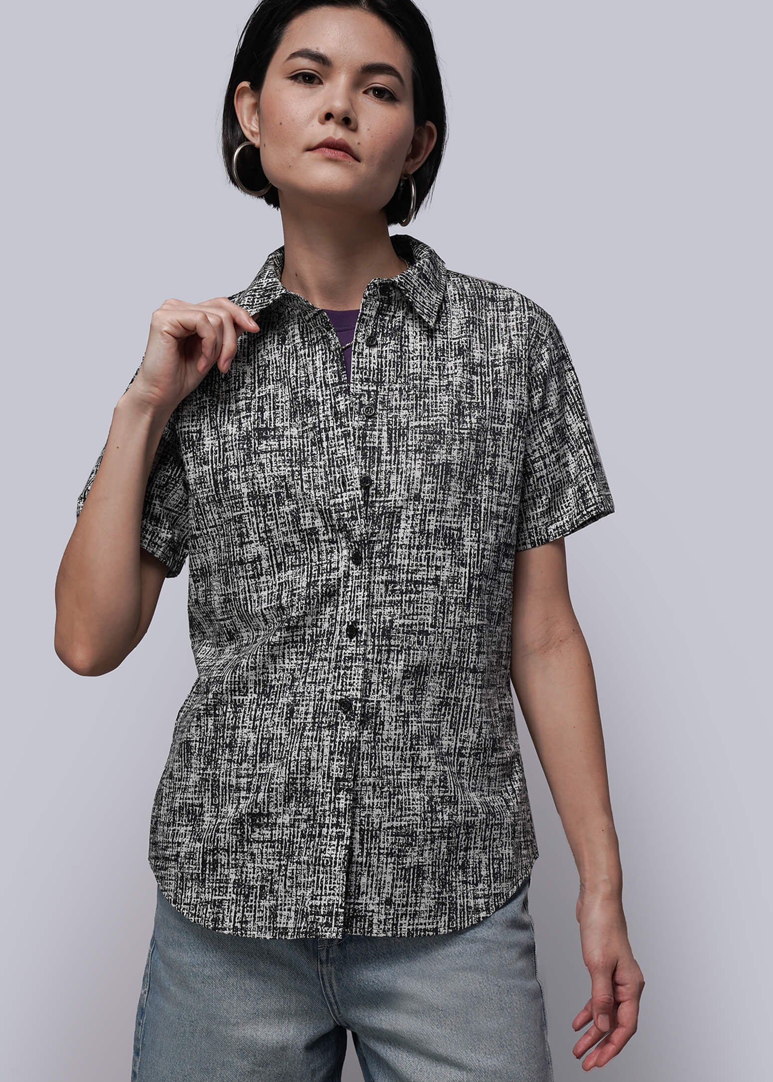 S=Woman wearing a patterned shirt and light blue pants against a plain background