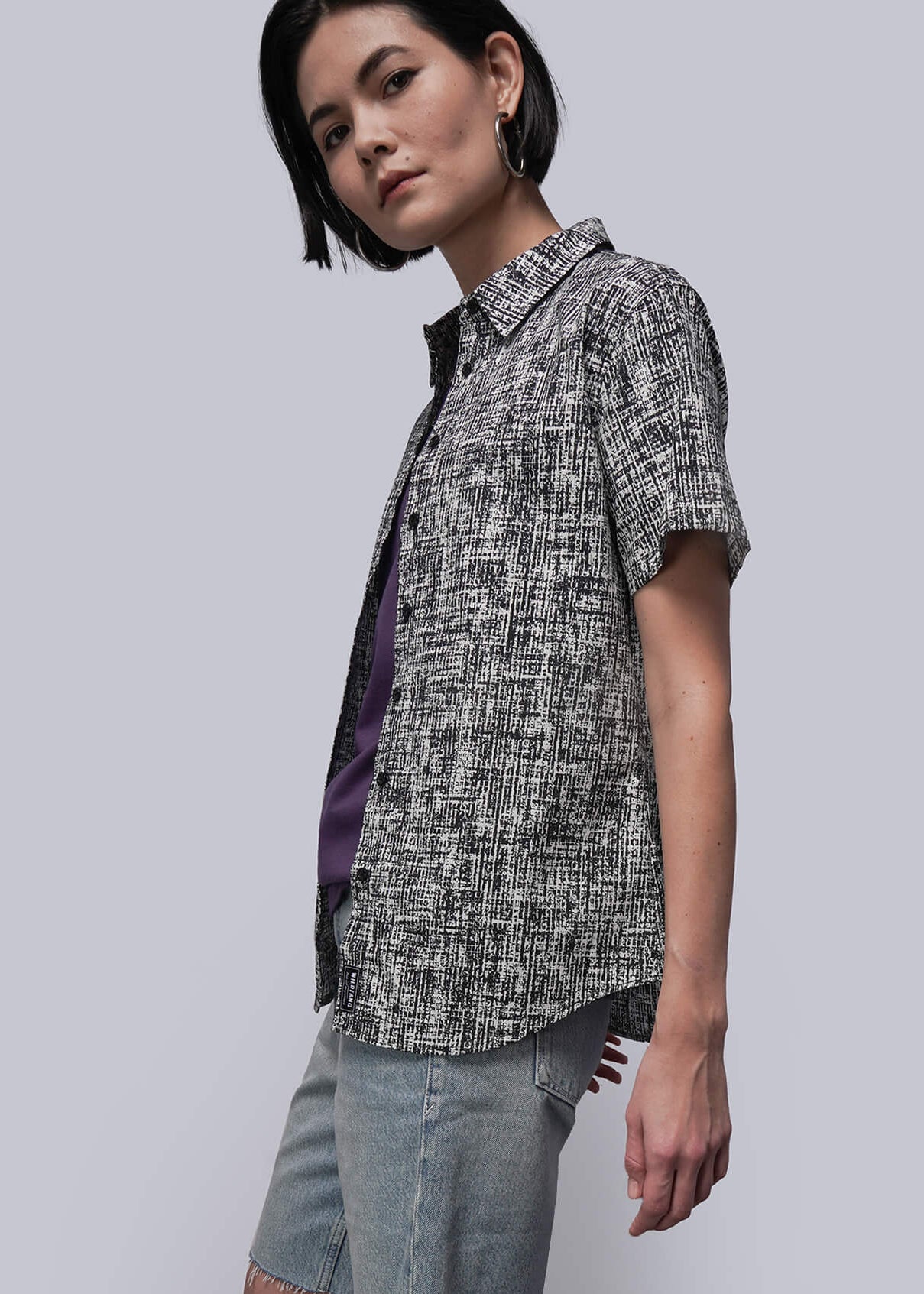 S=Person wearing a patterned shirt, denim shorts, and black boots against a plain background