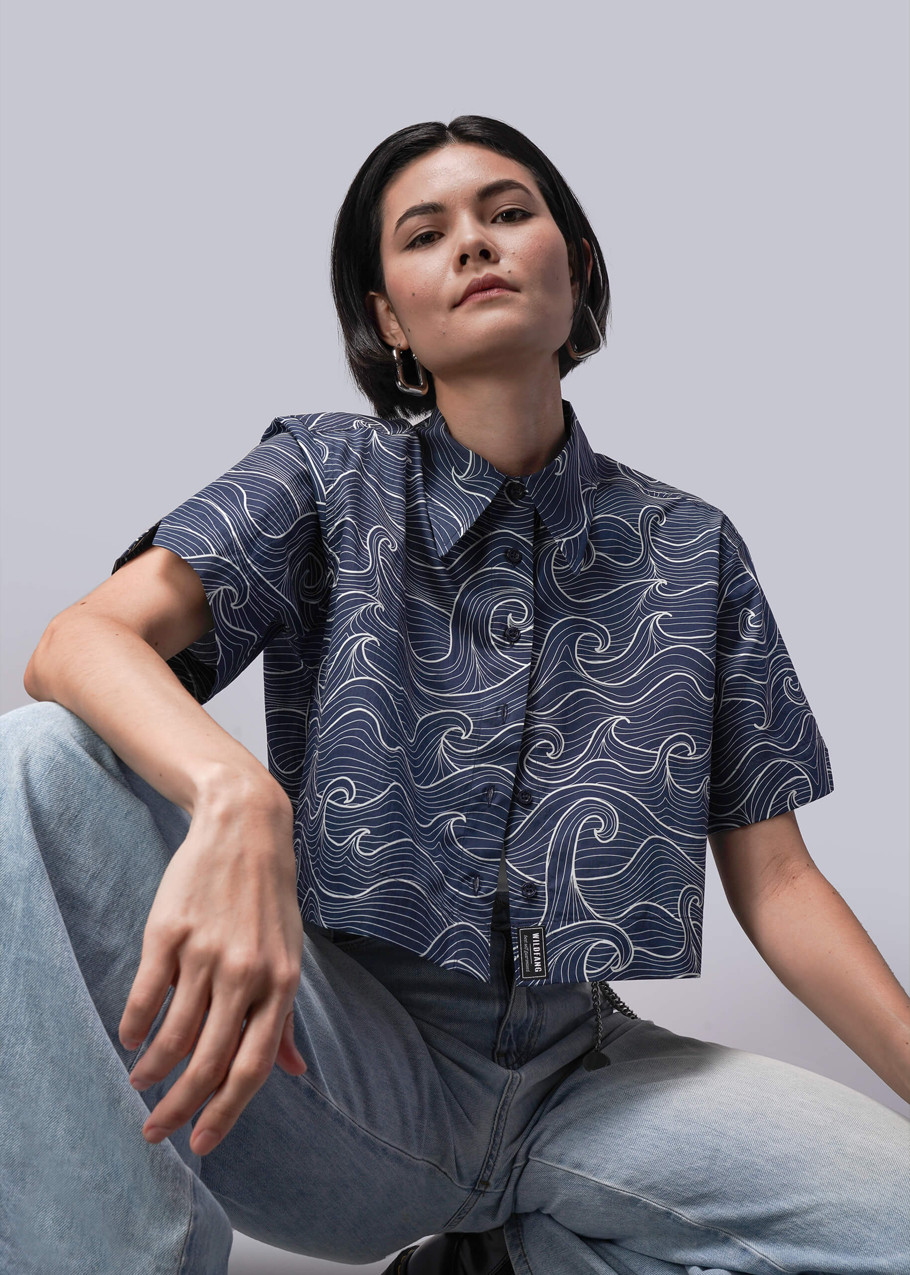 S=Person wearing a patterned navy shirt sitting against a light gray background