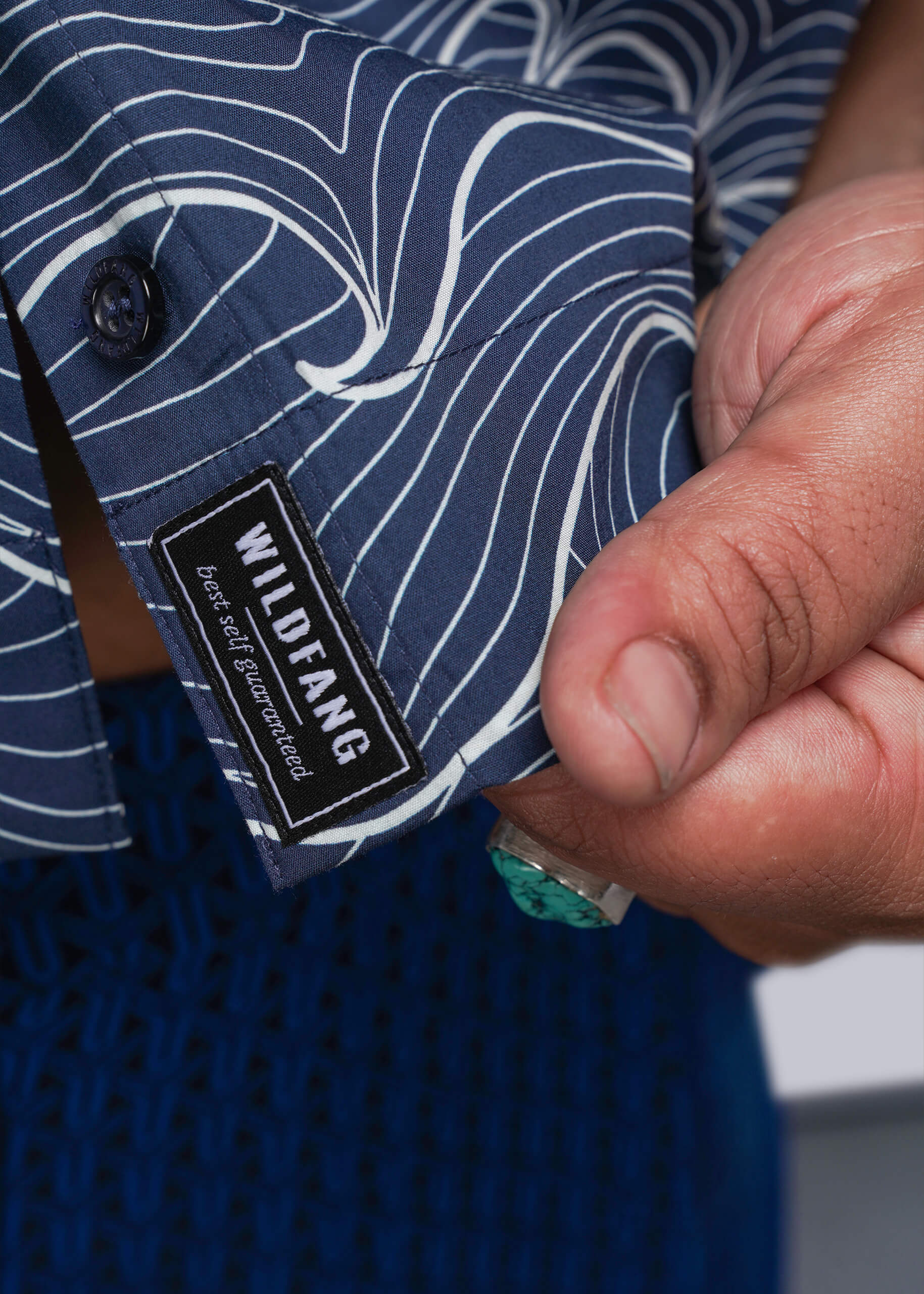 1X=Close-up of a person holding a blue shirt with a Wildfang label.