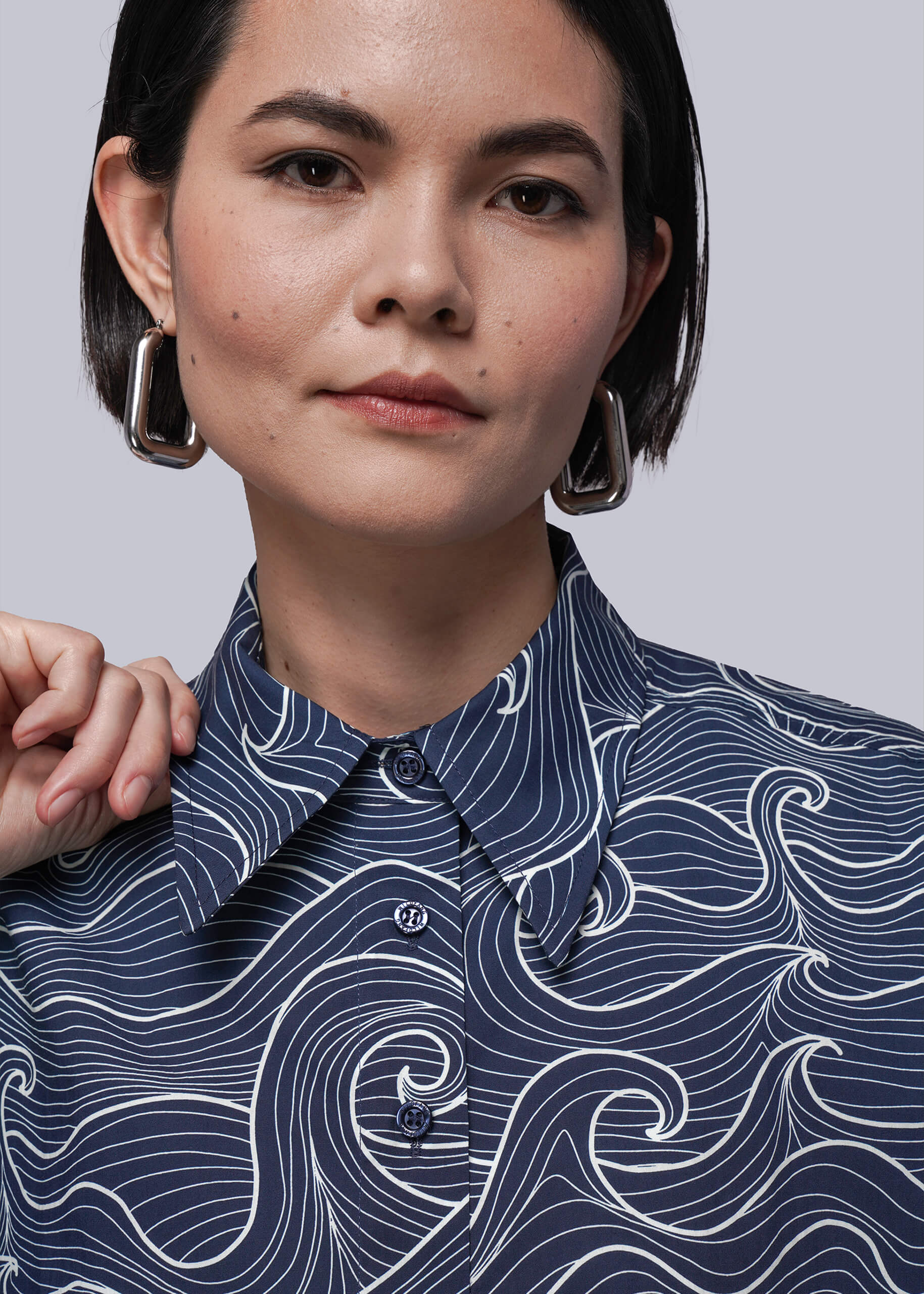 S=Woman wearing a navy blue shirt with white wave pattern against a gray background