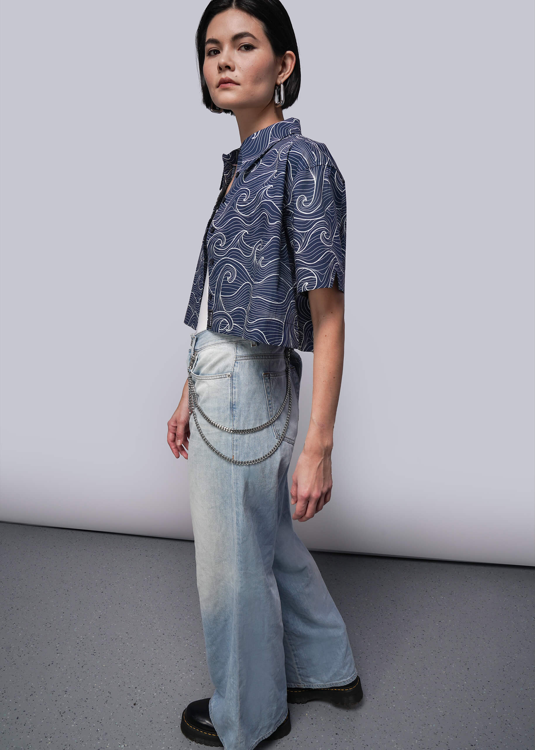 S=Person wearing a patterned shirt and light blue jeans against a plain background