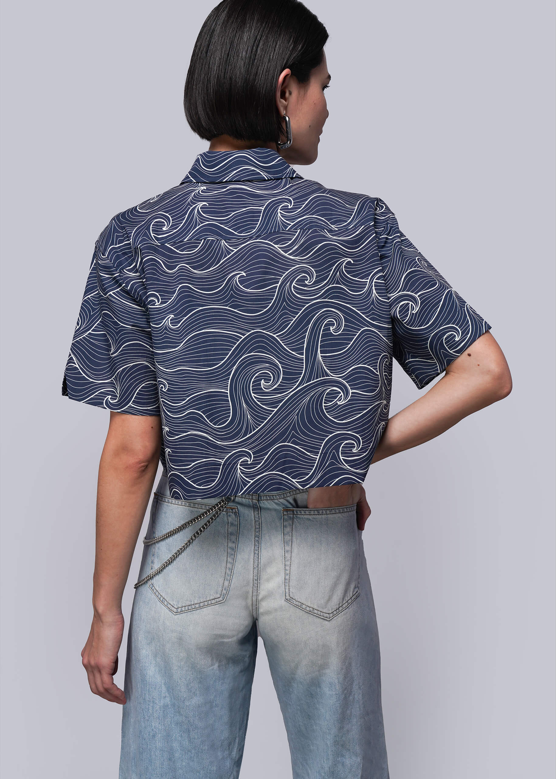 S=Person wearing a blue patterned shirt and light blue jeans on a gray background