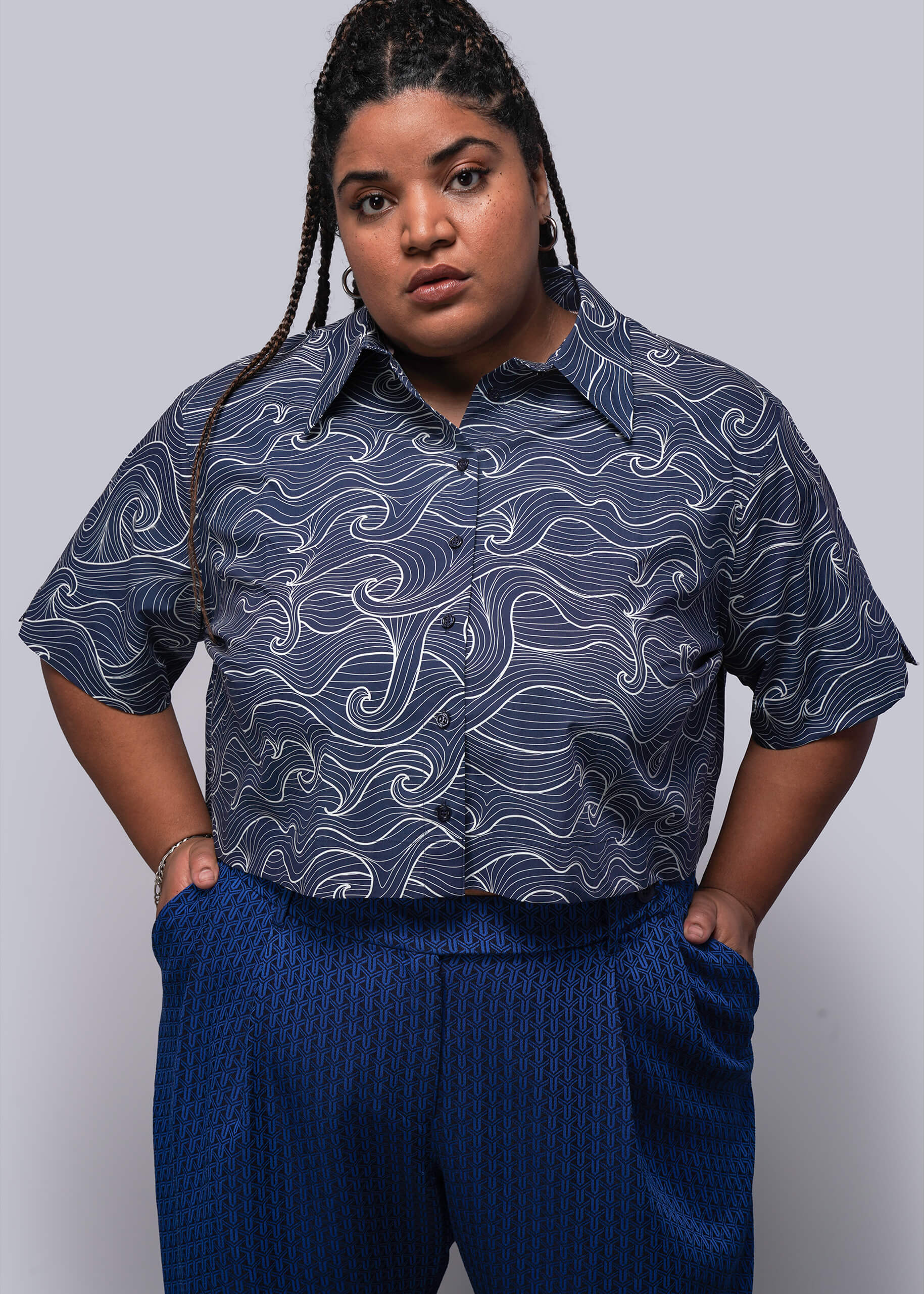 1X=Person wearing a patterned blue shirt and blue pants against a gray background