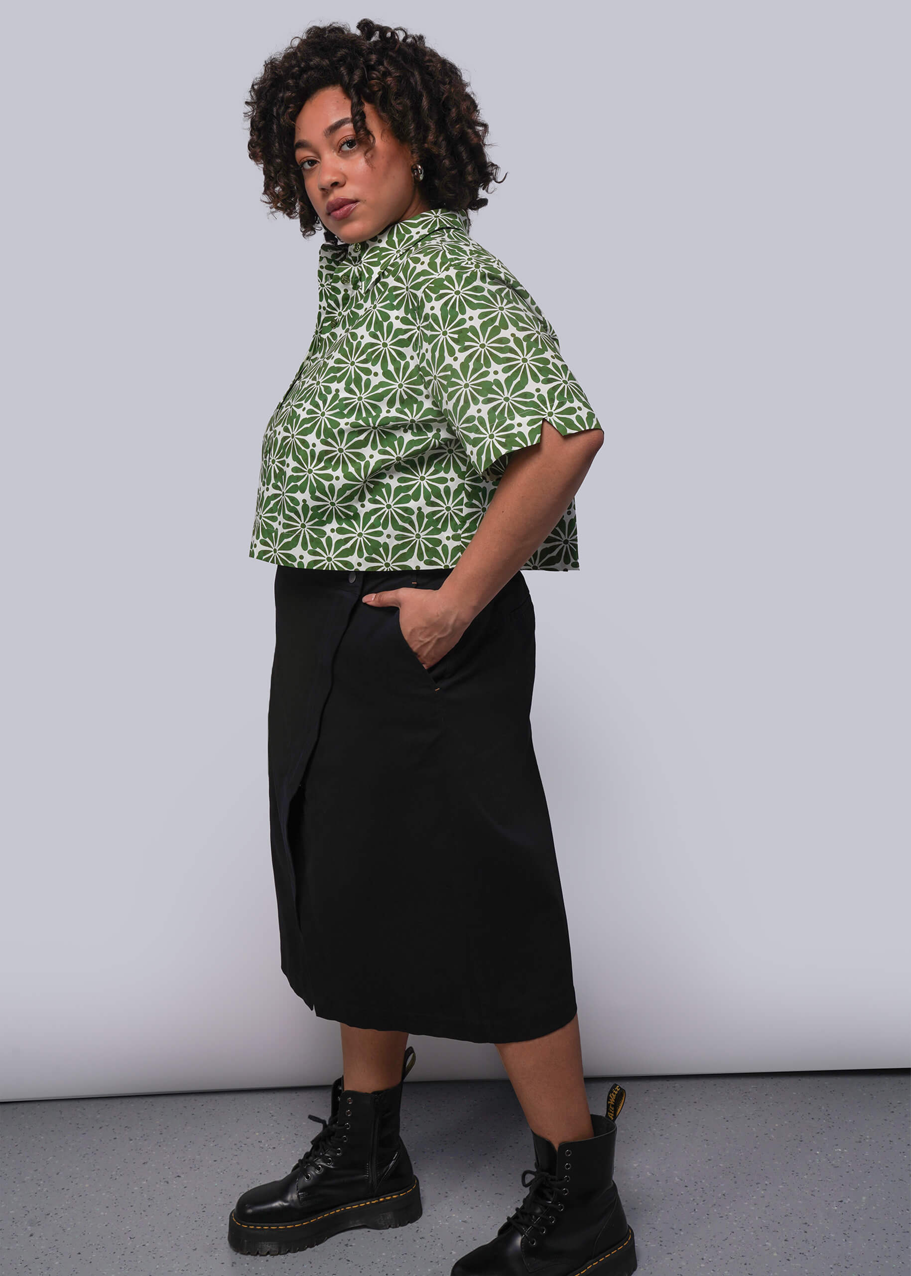 1X=Person wearing a green patterned shirt and black skirt against a white background