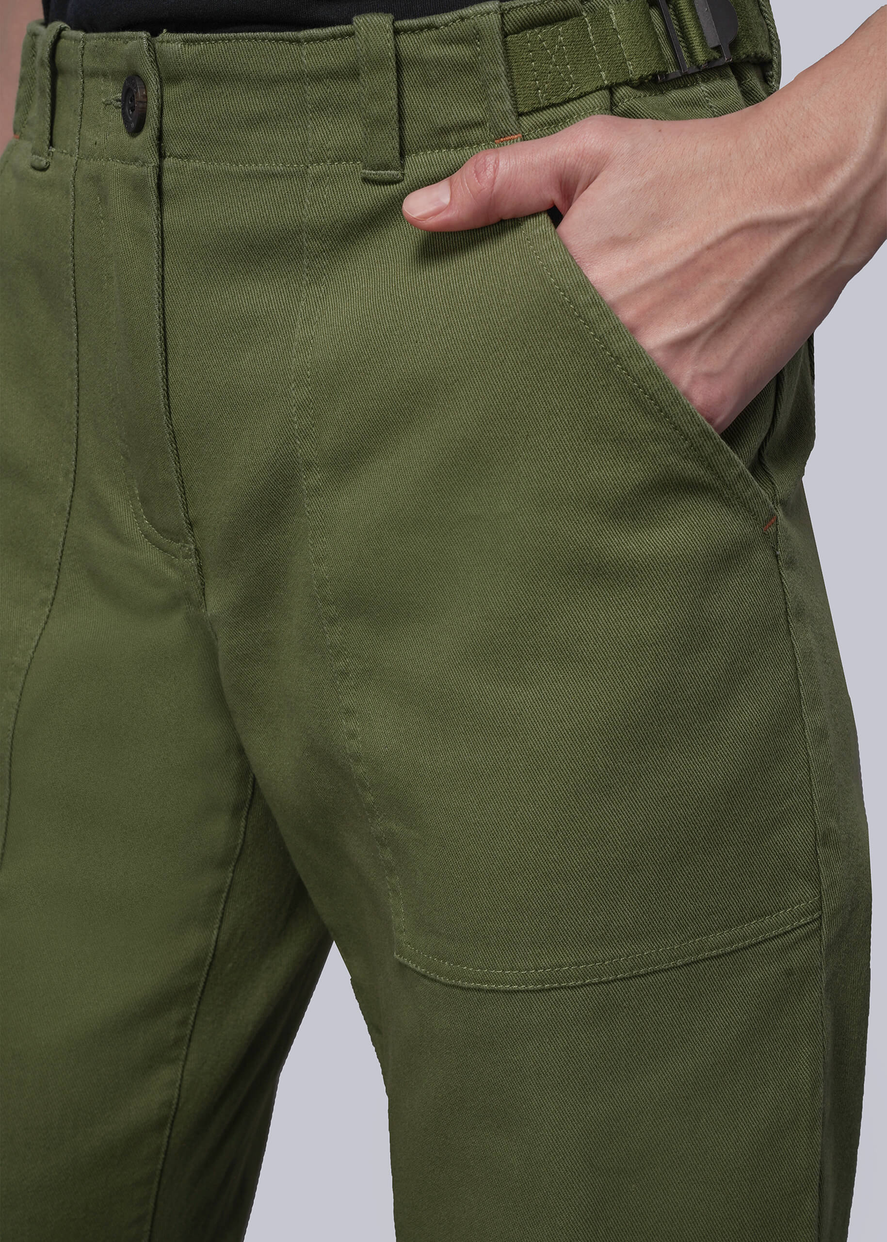 Close-up of green pants with a hand in the pocket on a light gray background