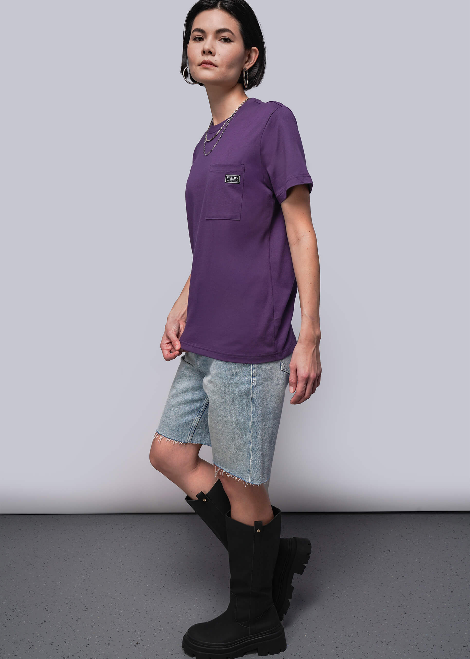 S=Person wearing a purple t-shirt, denim shorts, and black boots on a plain background