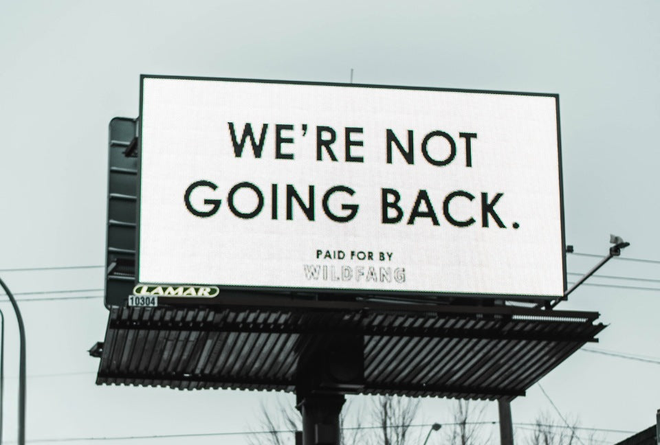 Picture of billboard with black text on white background that says "We're not going back. Paid for by Wildfang"