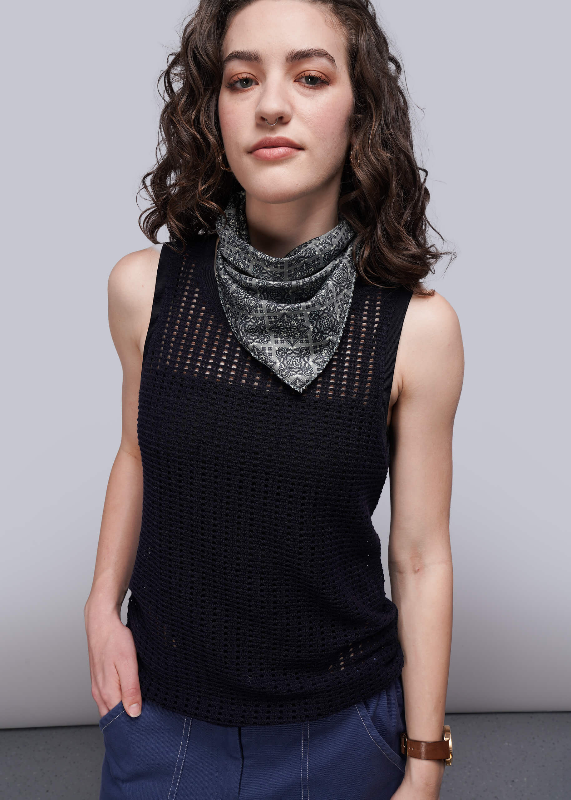Woman wearing a black sleeveless knit mesh top with a patterned scarf against a plain background