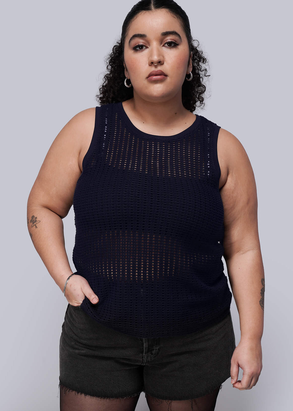 1X=Woman wearing a navy blue knit mesh sleeveless top with intricate detailing on a plain background