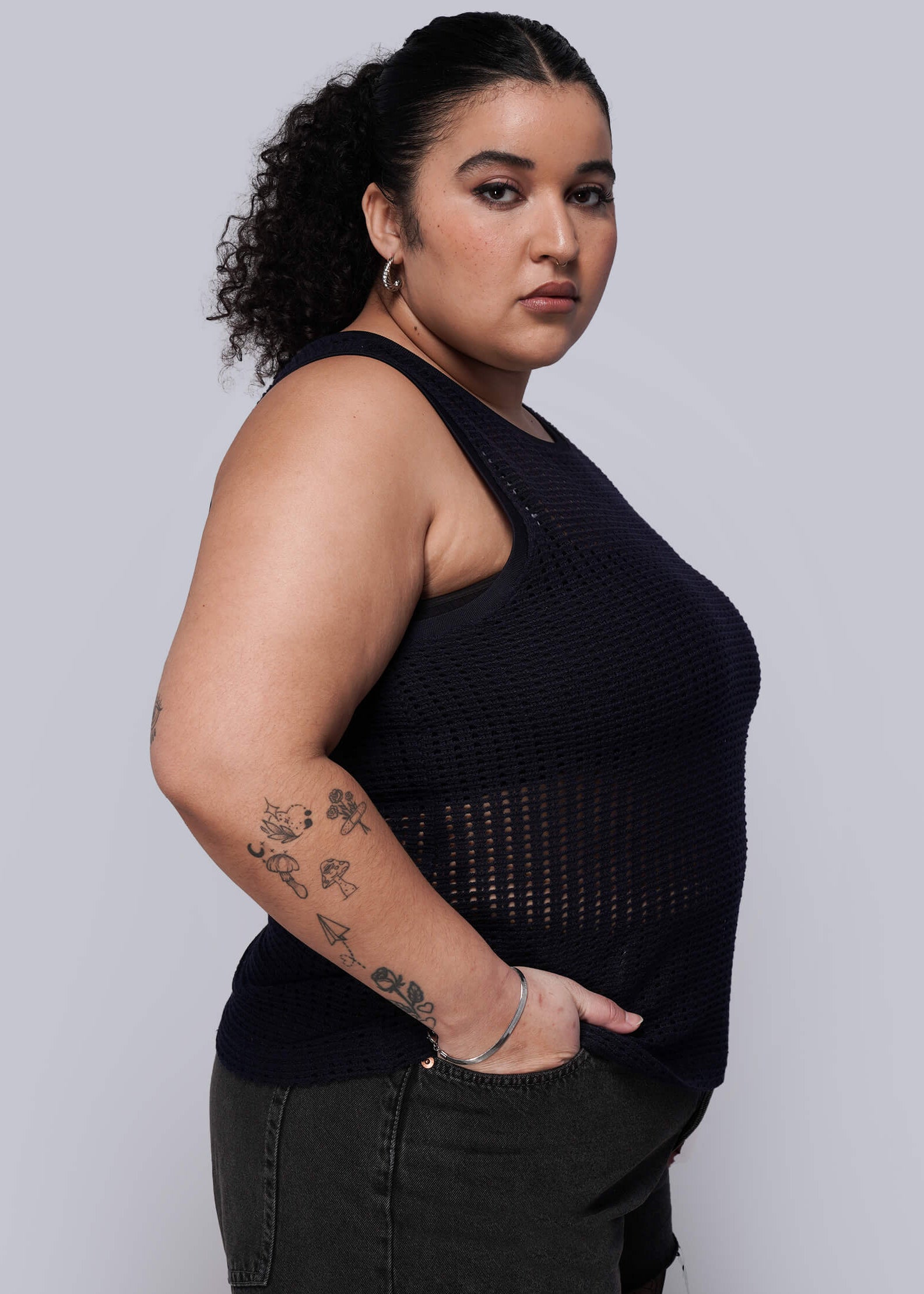 1X=Woman wearing a navy blue knit mesh sleeveless top against a plain background