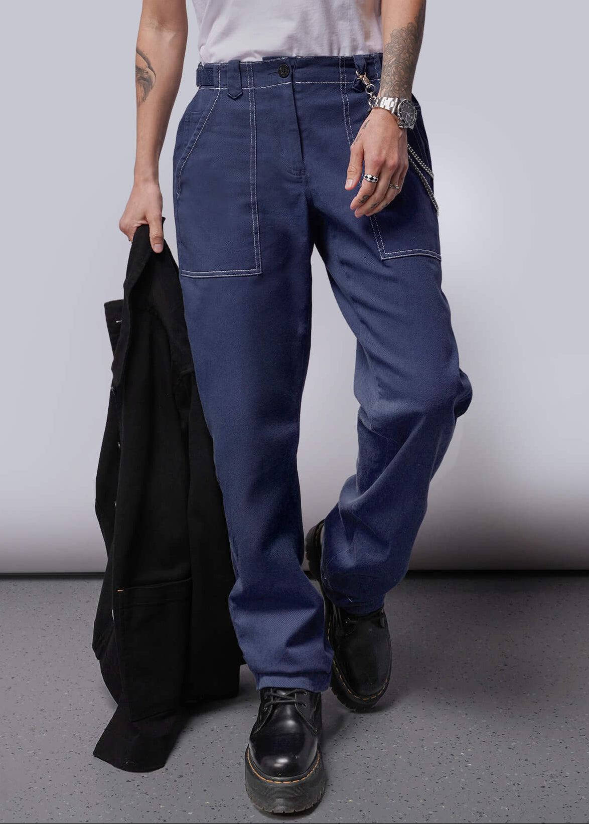 S=Person wearing a white sleeveless shirt and blue pants holding a black jacket against a plain background