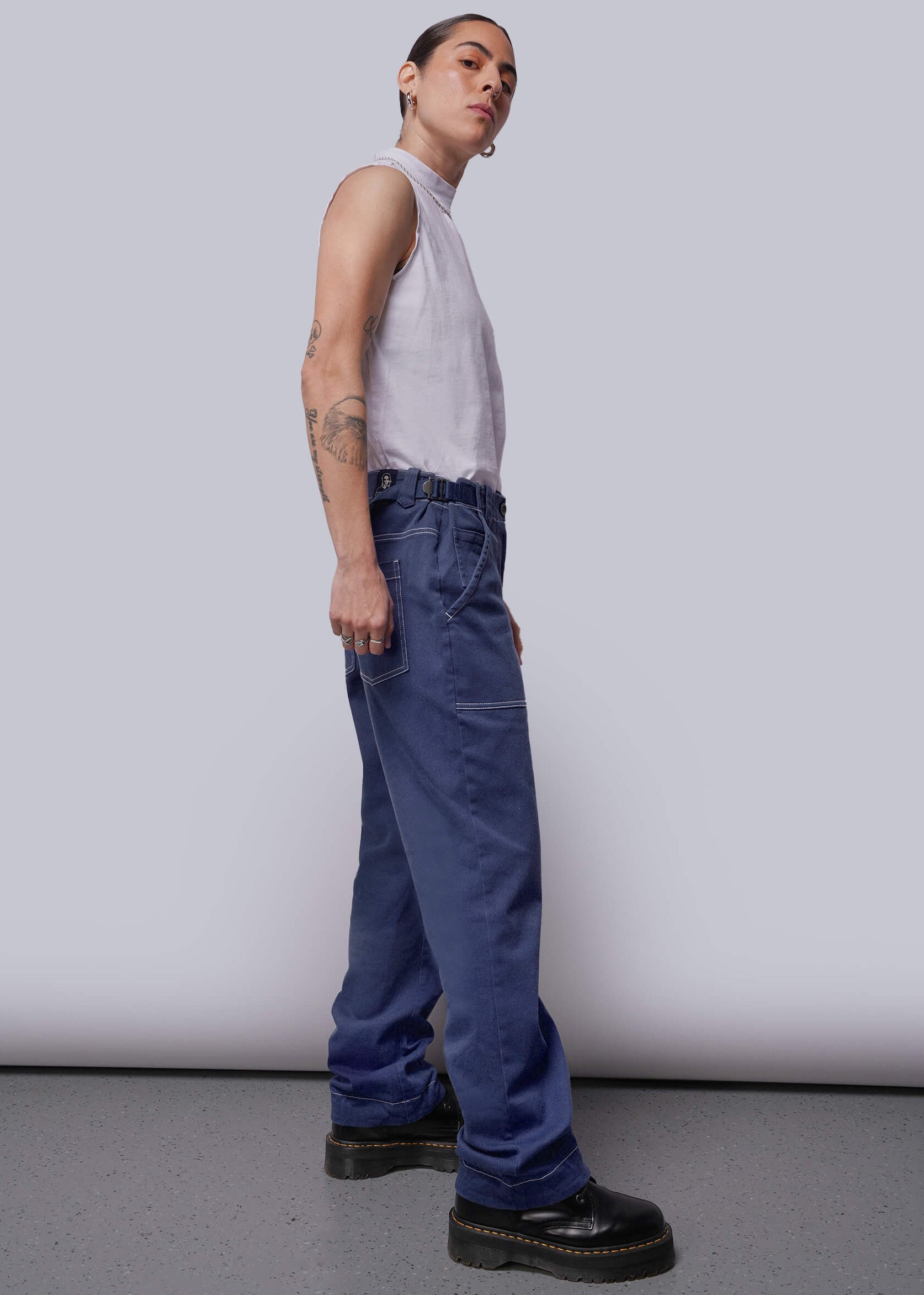 S=Person wearing a white sleeveless shirt and blue jeans standing against a plain background