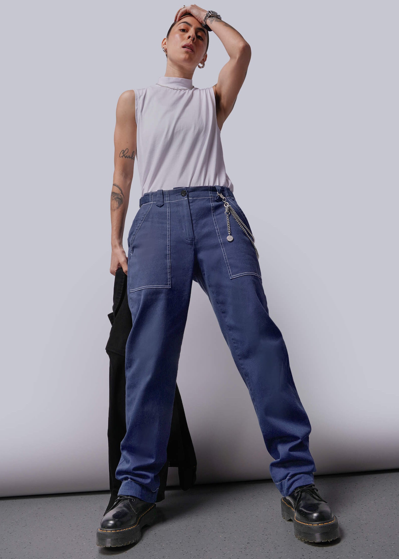 Person wearing a white sleeveless top and blue denim pants against a plain background