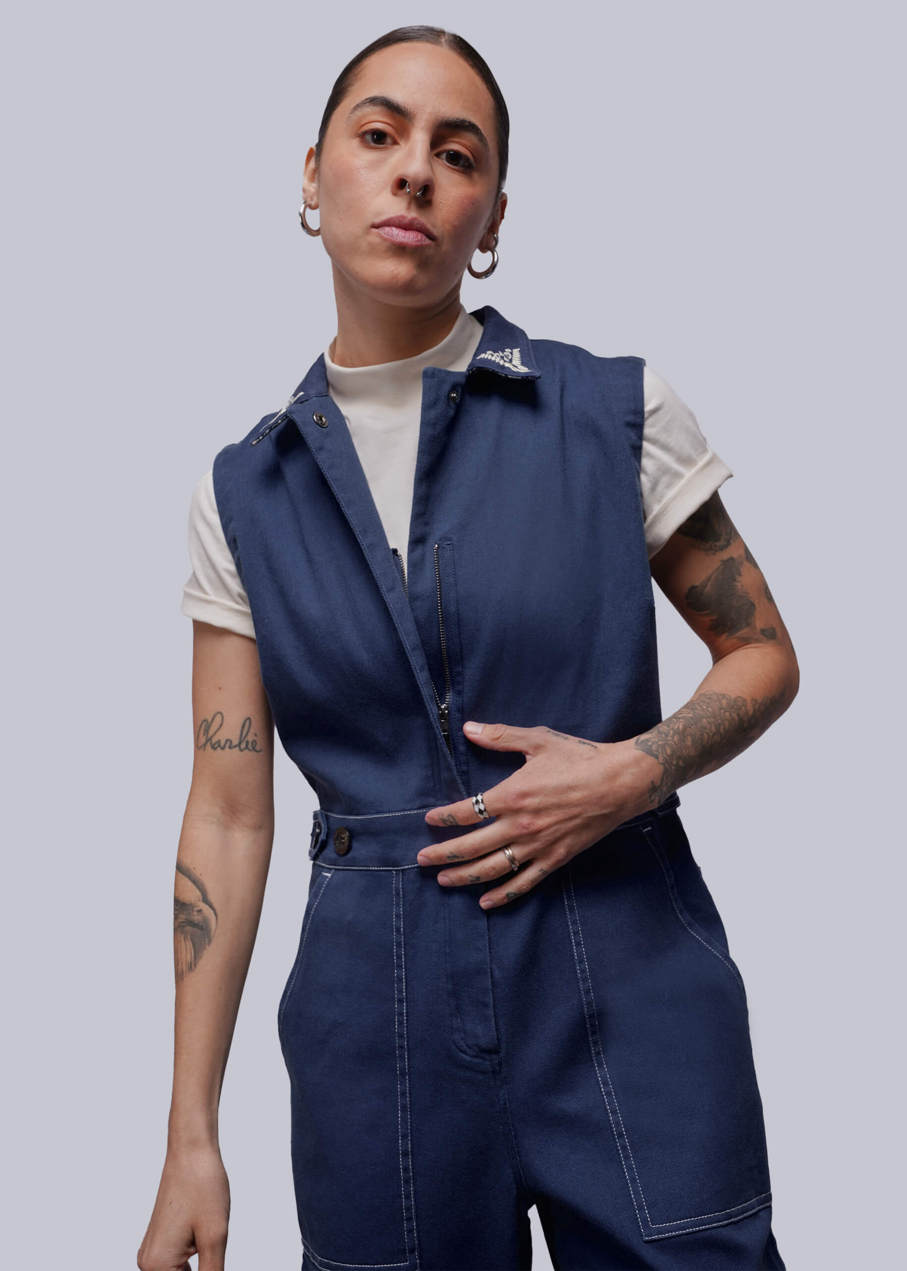 S=Person wearing a blue sleeveless jumpsuit with a white shirt underneath on a light gray background