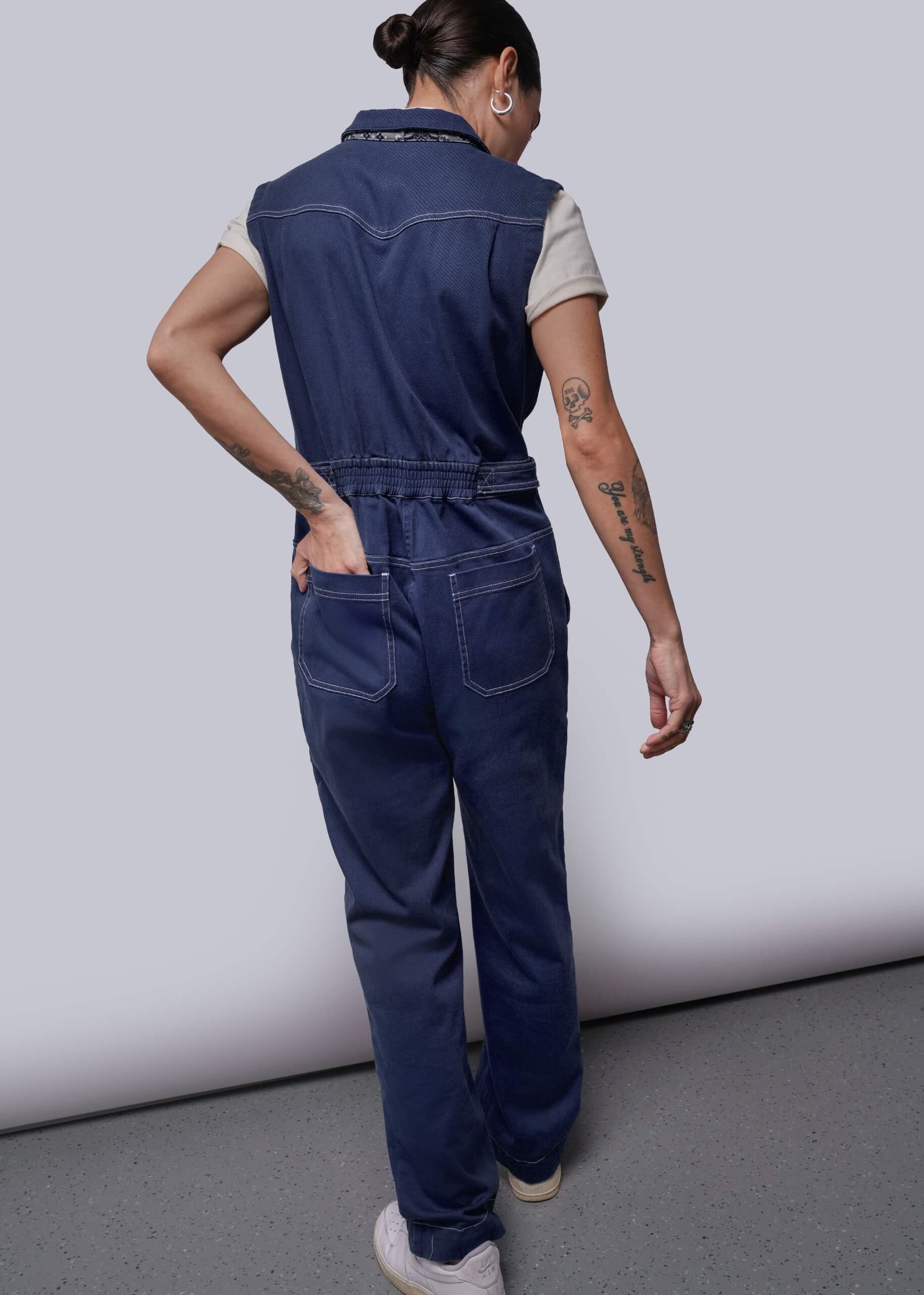 S=Back of person wearing a blue denim jumpsuit against a plain background