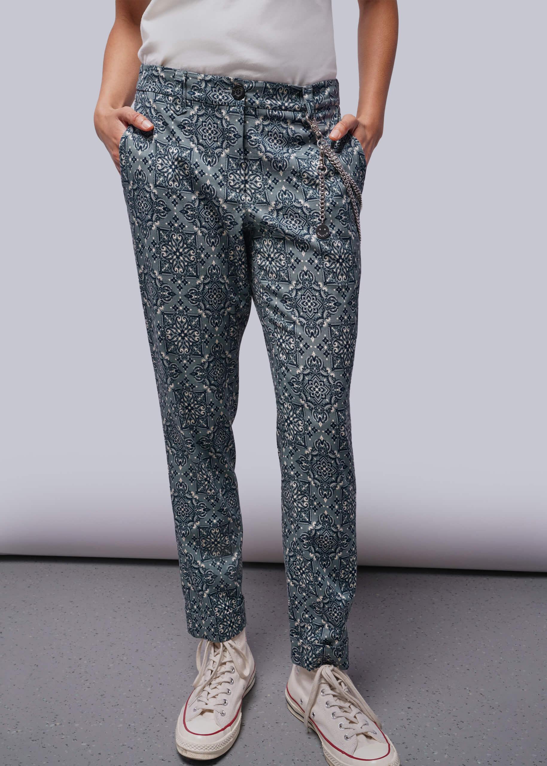 Person wearing blue patterned pants and white sneakers on a plain background