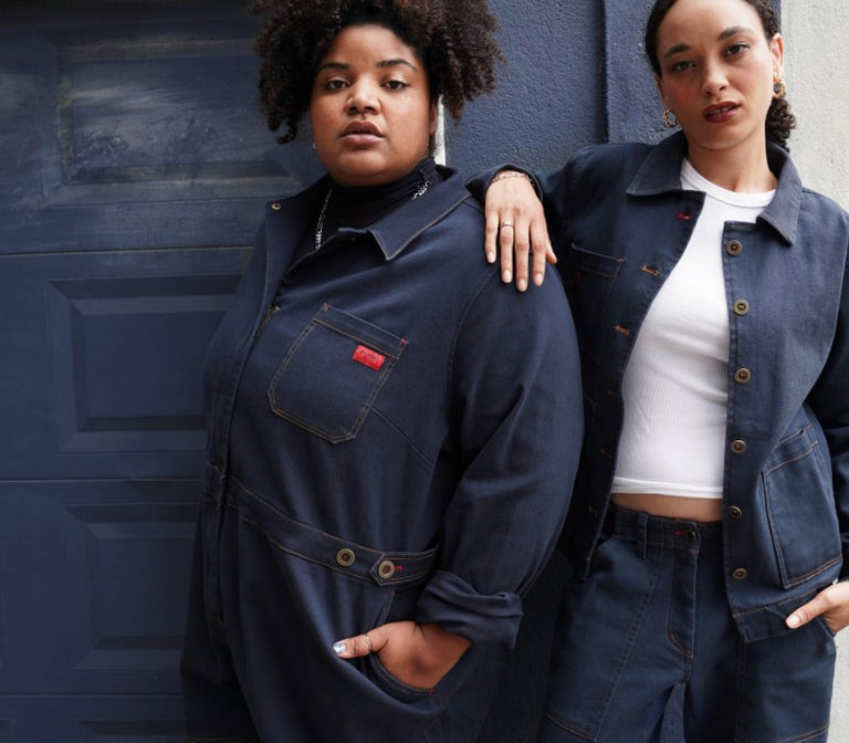 Two people wearing blue denim outfits stand in front of blue garage door.