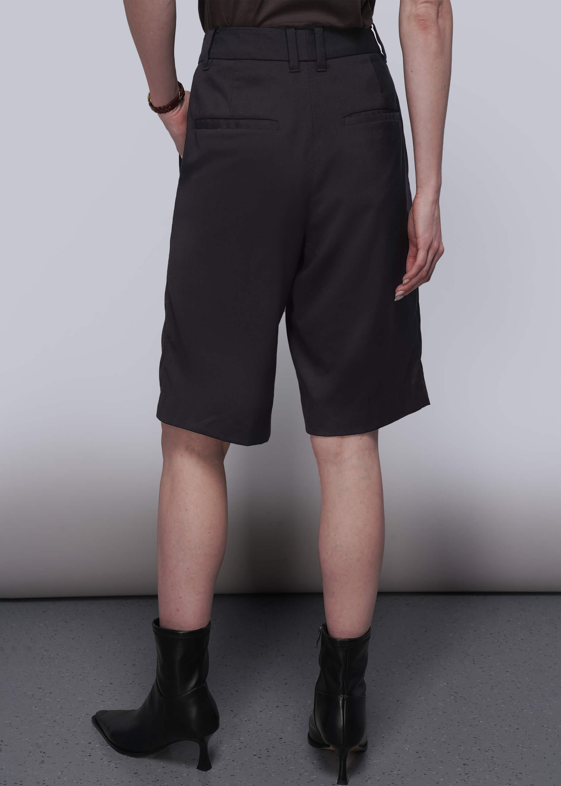 S=Pictured from the back, a person wearing black shorts and black boots against a plain background
