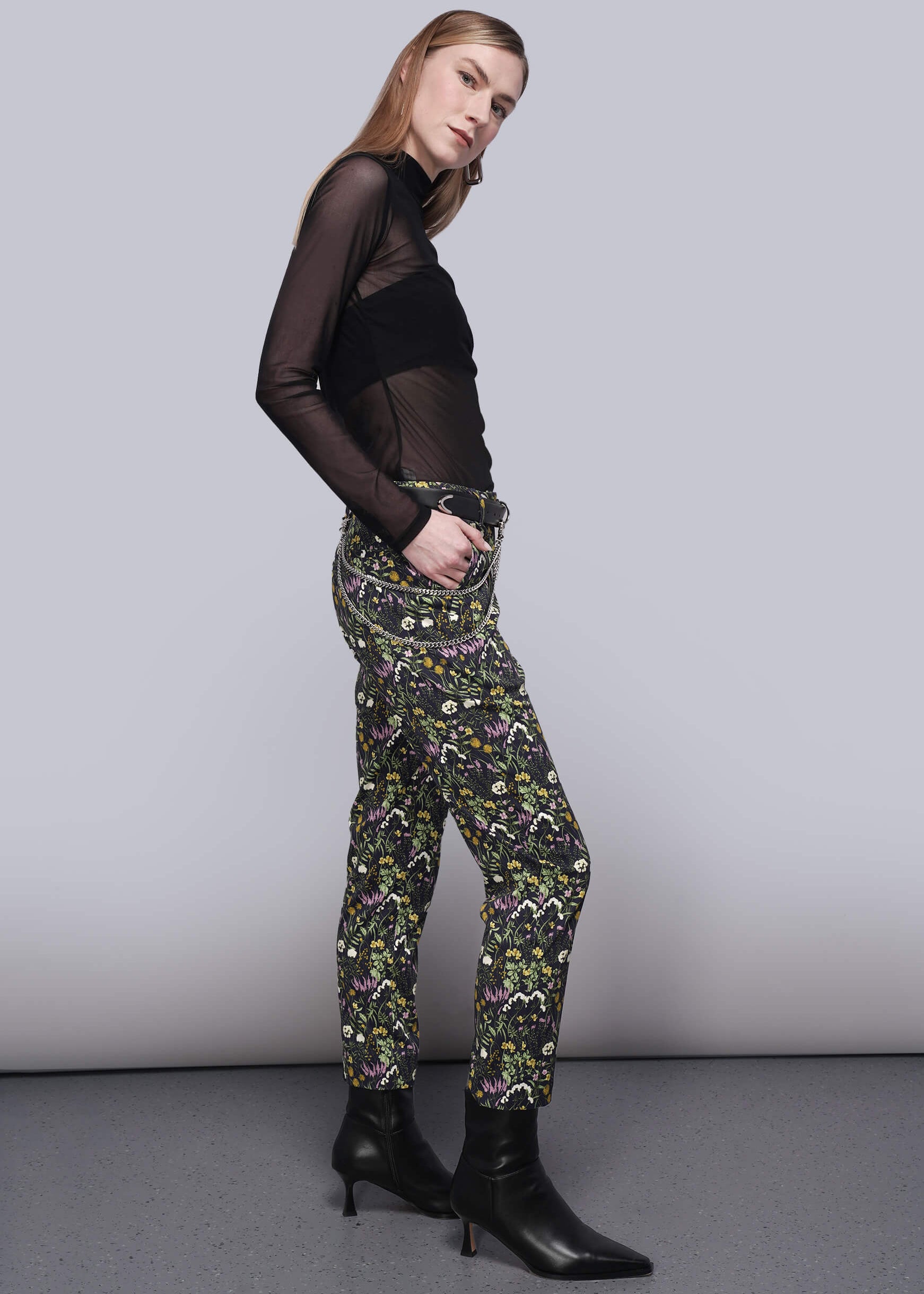 S=Woman wearing a black sheer top and patterned pants against a plain background