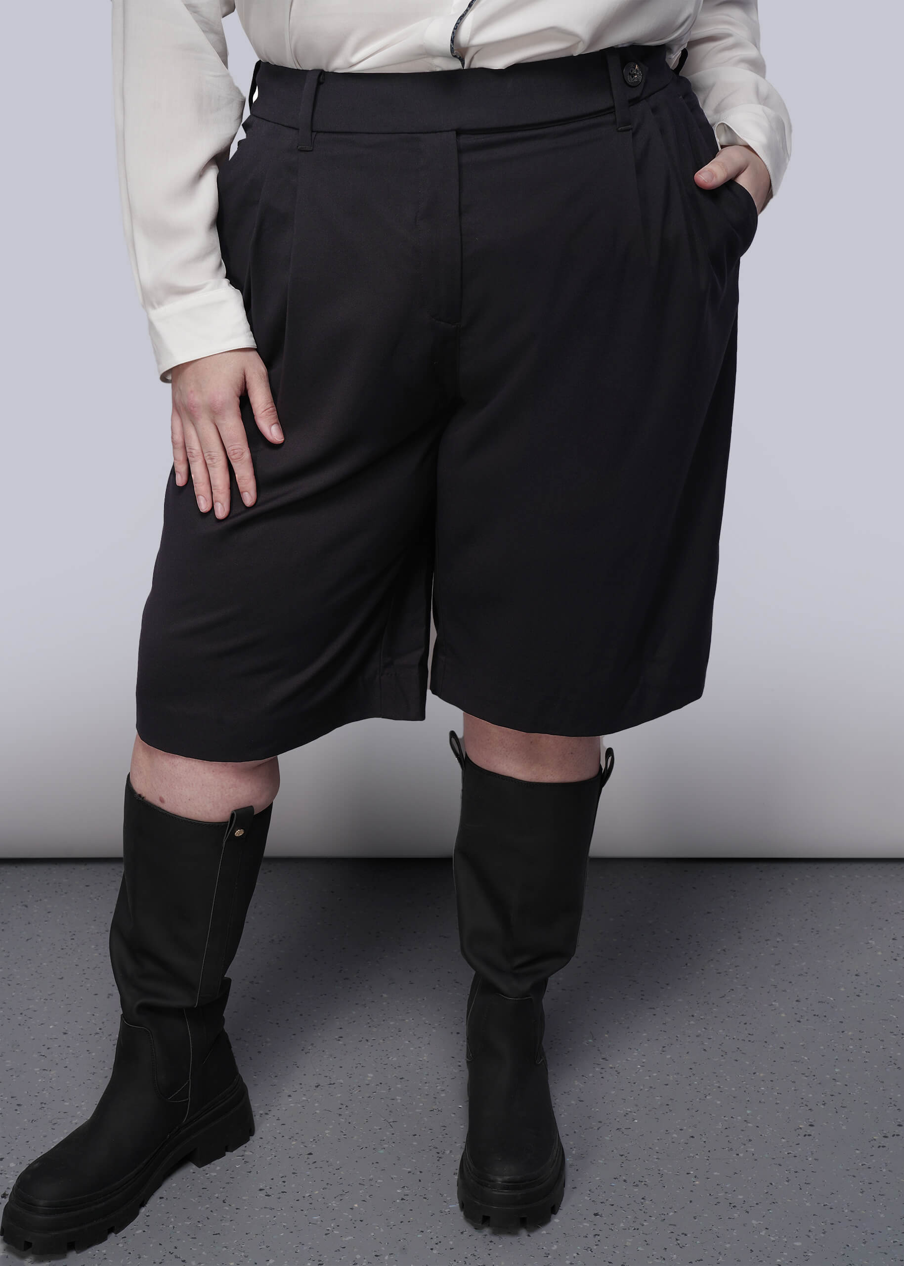 1X=Person wearing black high-waisted shorts and black boots on a plain background
