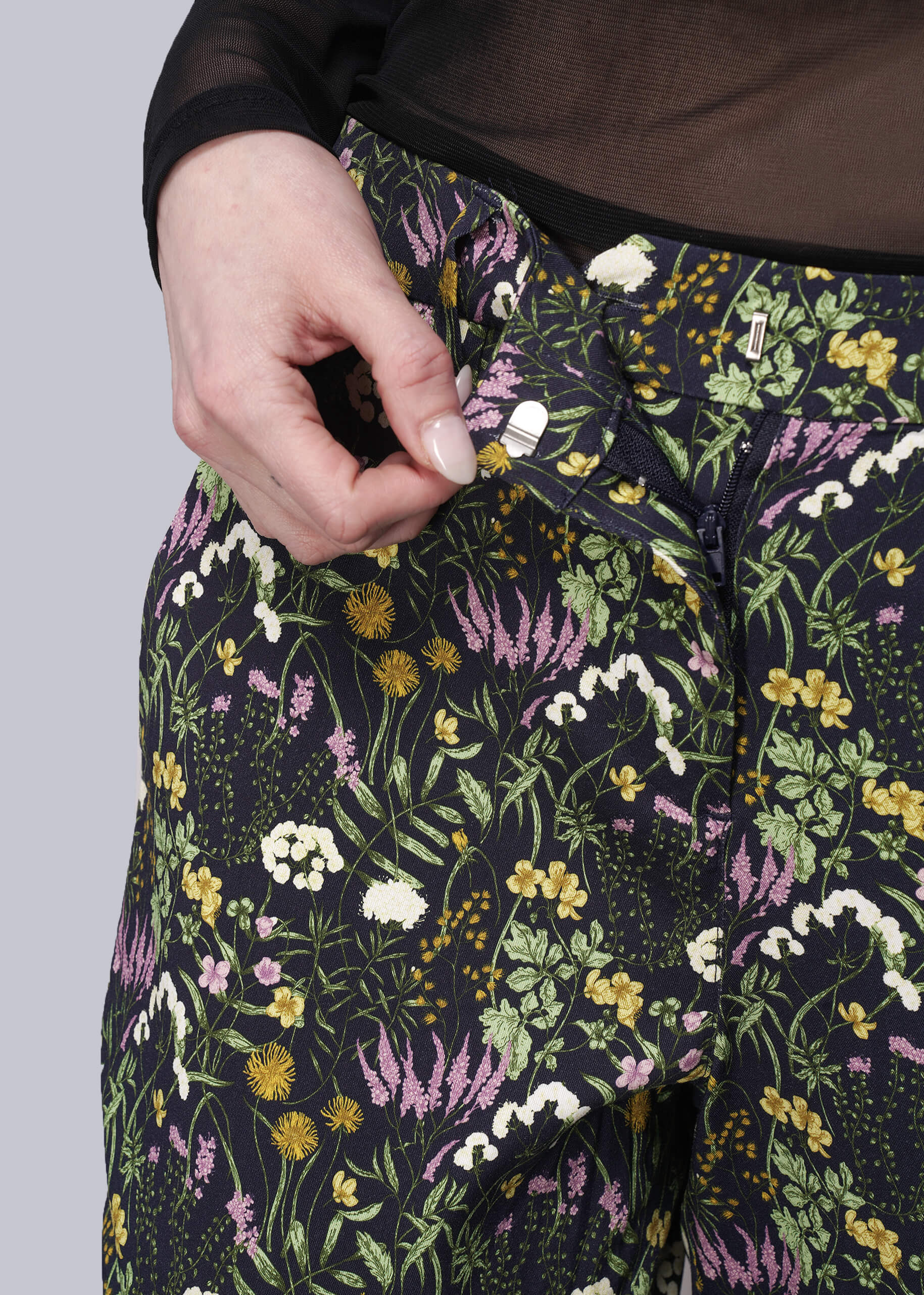 Floral-patterned pants with a hand adjusting the waistband against a neutral background